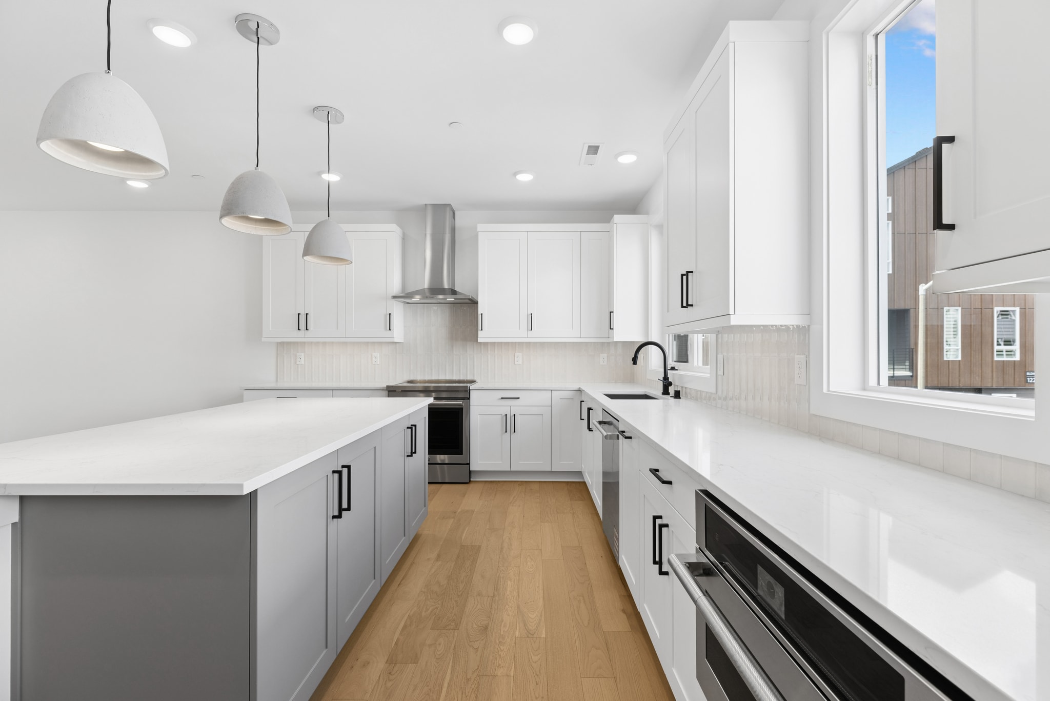 A modern, minimalist kitchen with white cabinets, gray countertops, and pendant lighting fixtures, set against a bright and airy backdrop.