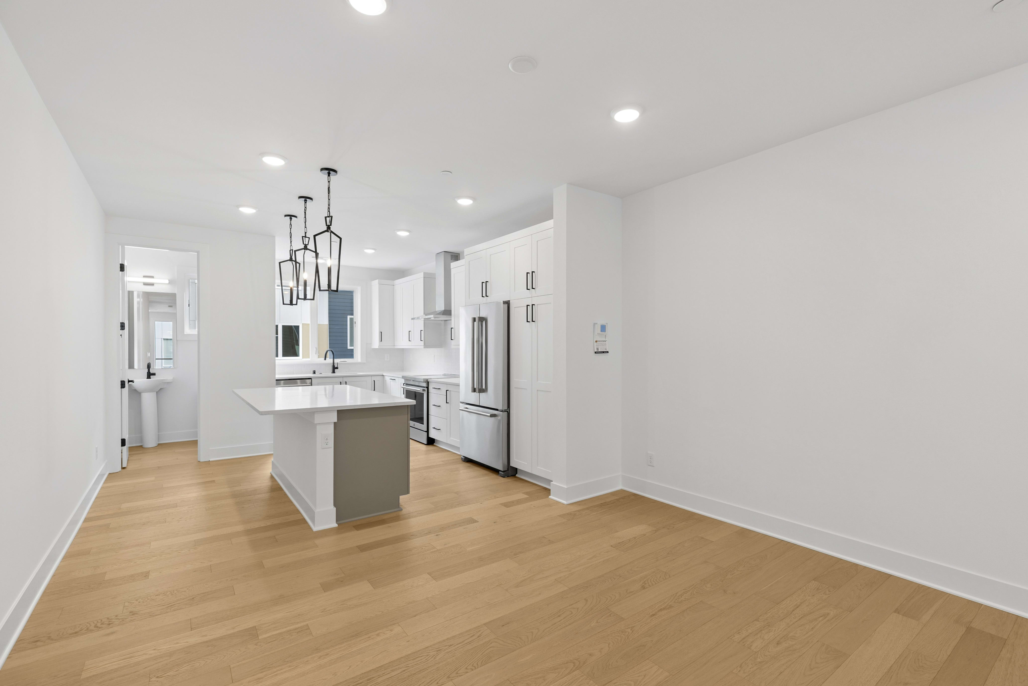 A modern, open-concept kitchen with white walls, hardwood floors, and sleek appliances, featuring a central island and pendant lighting.