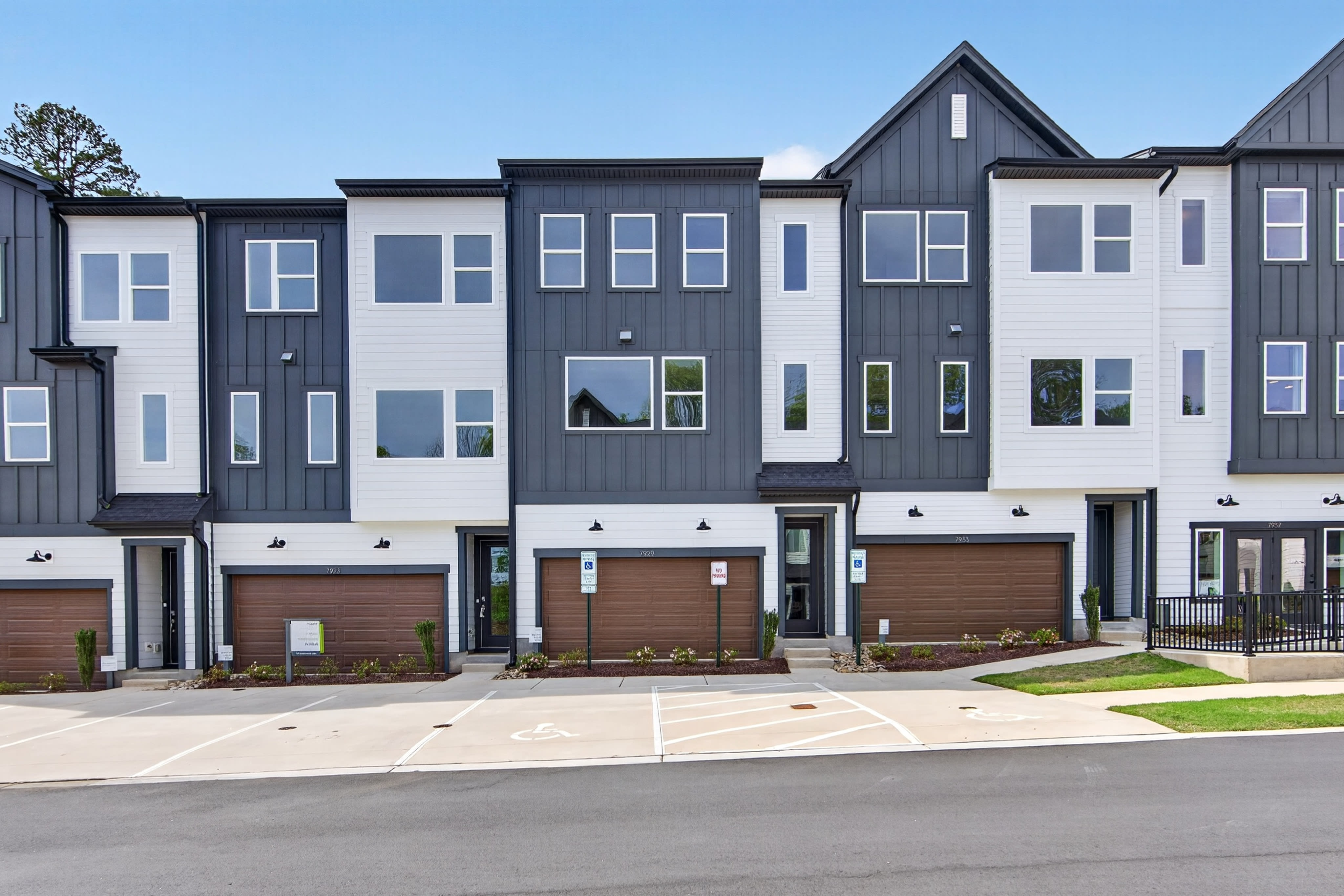 A row of modern, multi-story townhouses with a mix of gray and brown siding, large windows, and attached garages, set against a clear blue sky.