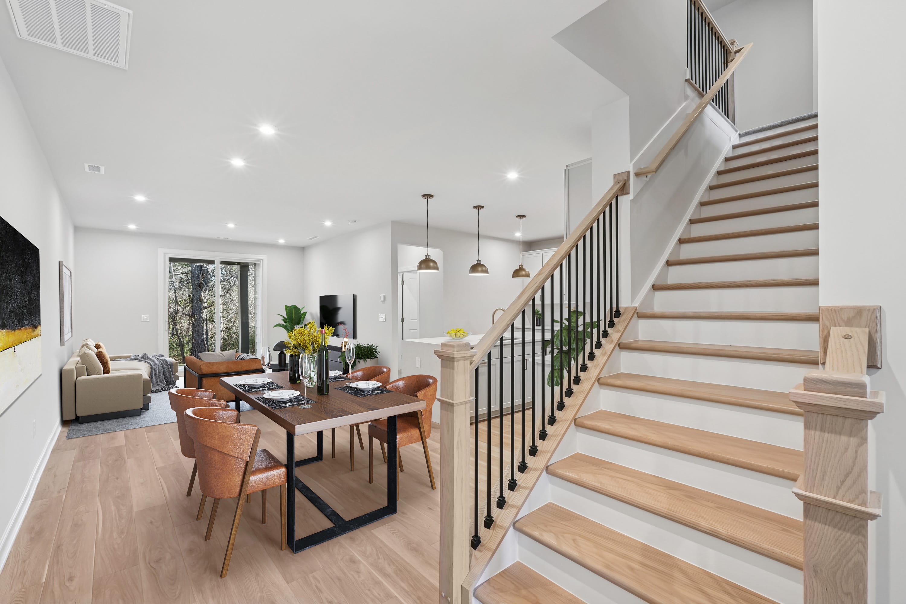 A modern and spacious open-concept living area with a dining table, leather chairs, and a staircase leading to the upper level.