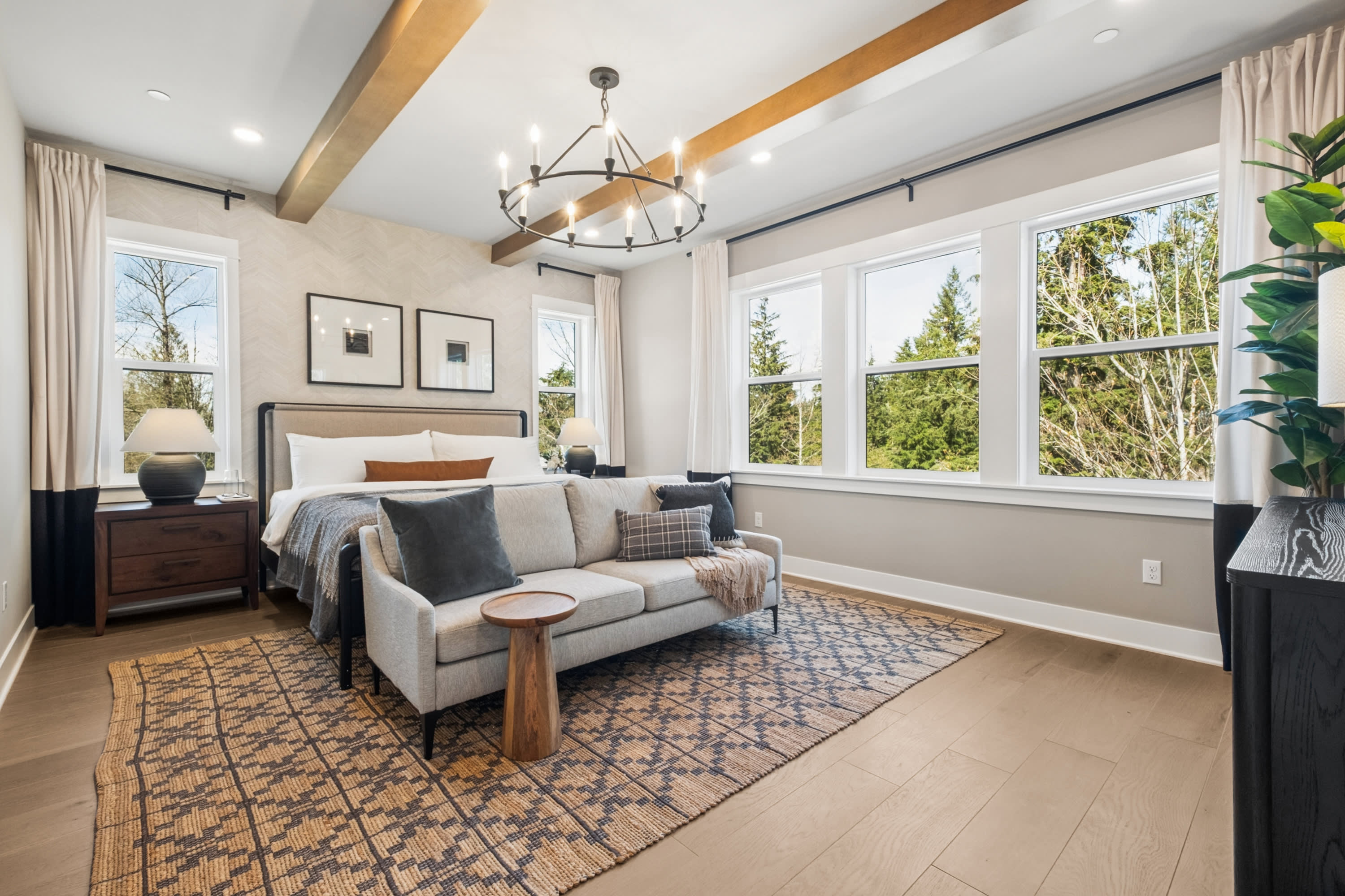 A spacious and well-designed bedroom with large windows, a cozy seating area, and a modern chandelier overhead, creating a warm and inviting atmosphere.