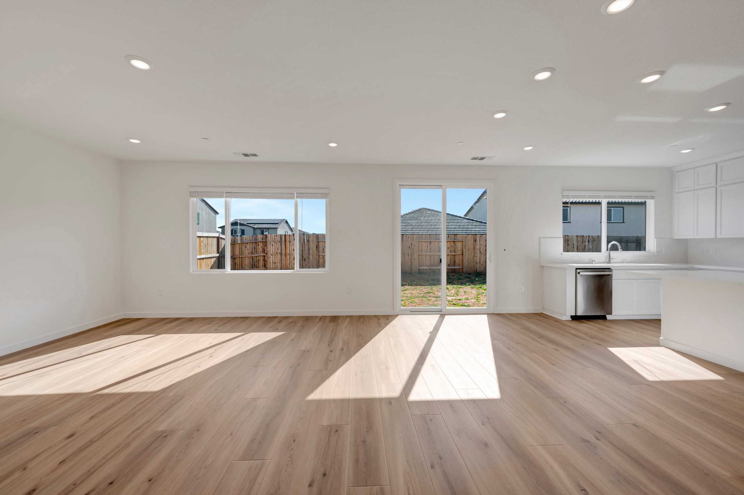 A spacious and bright interior with a wooden floor, large windows, and a kitchen visible in the background.