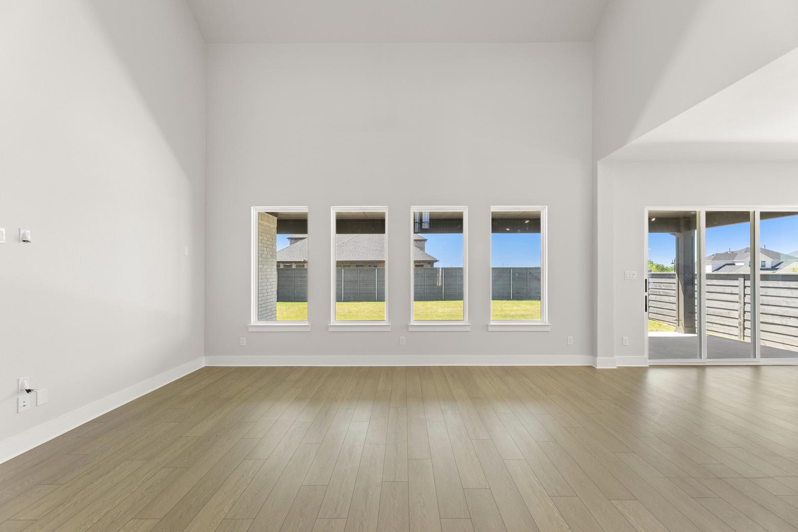 A spacious, minimalist room with large windows offering a view of the outdoors, featuring a hardwood floor and a clean, uncluttered interior.
