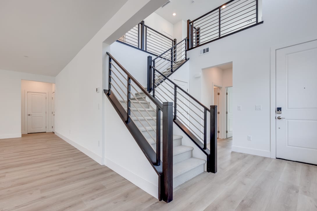 A modern, minimalist staircase with metal railings and wooden steps leads up to a second floor, with a plain white wall and a closed door visible in the background.