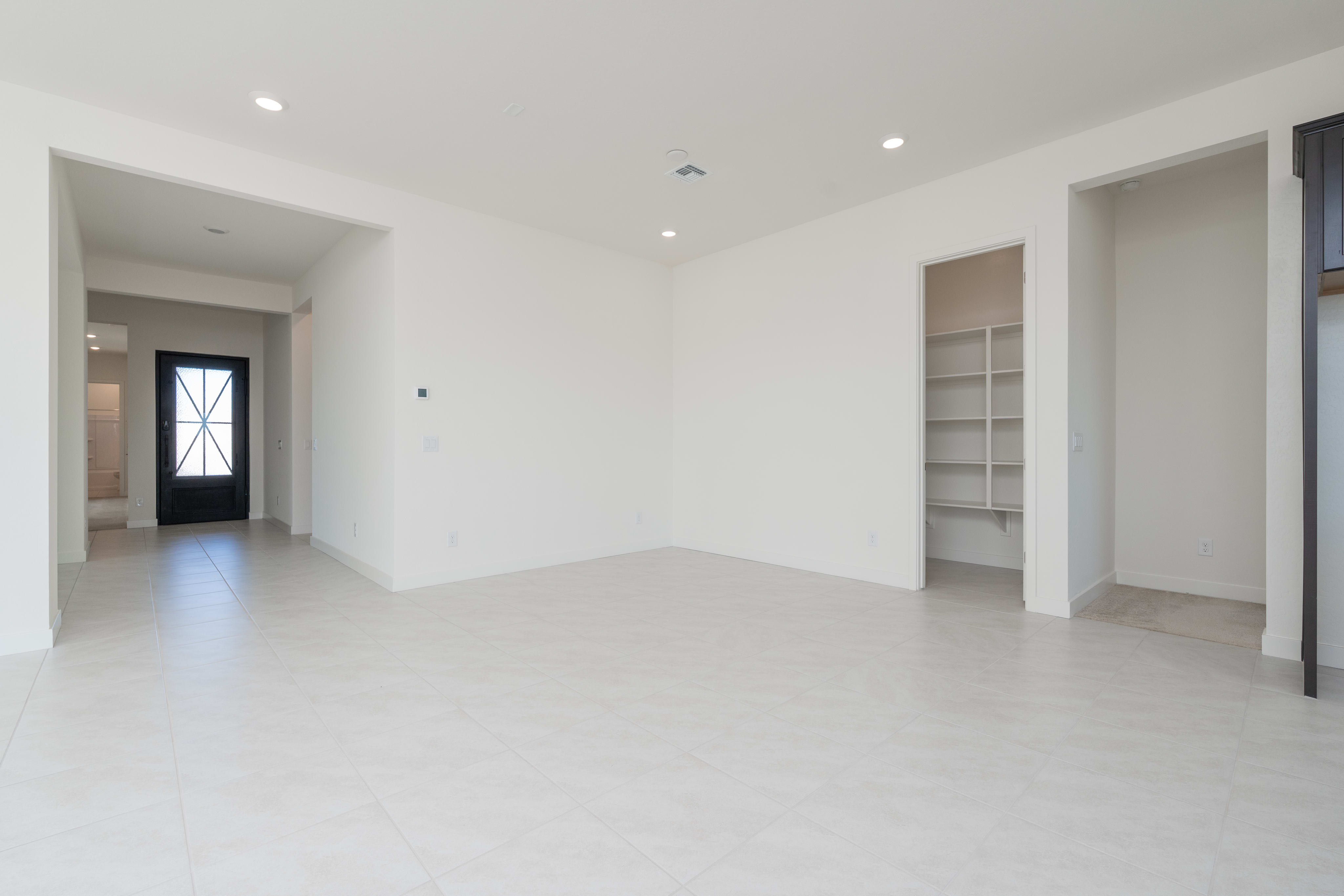 A spacious, minimalist room with white walls, a tiled floor, and a built-in shelving unit visible in the background.