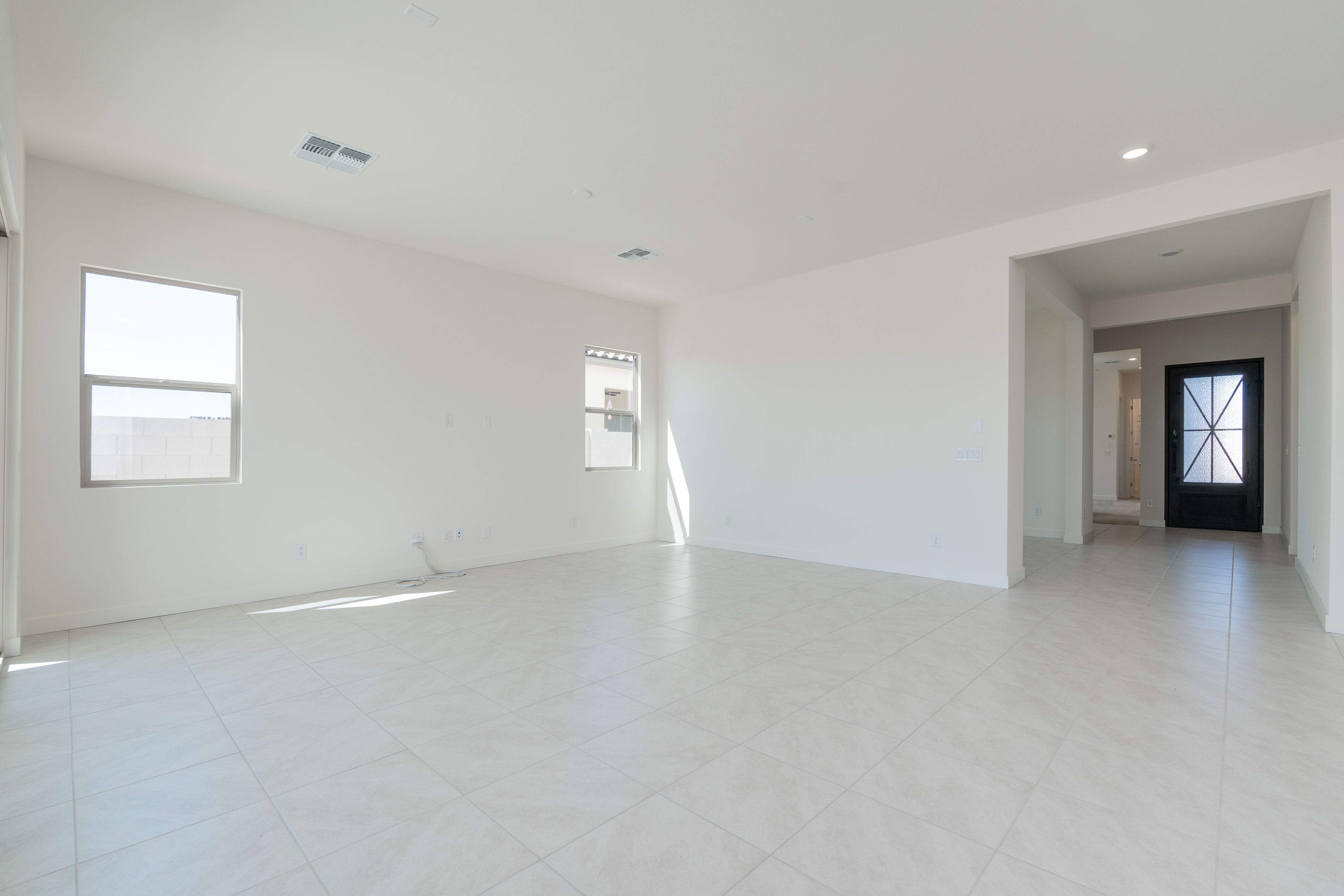 An empty, minimalist room with white walls, a large window, and a tiled floor.