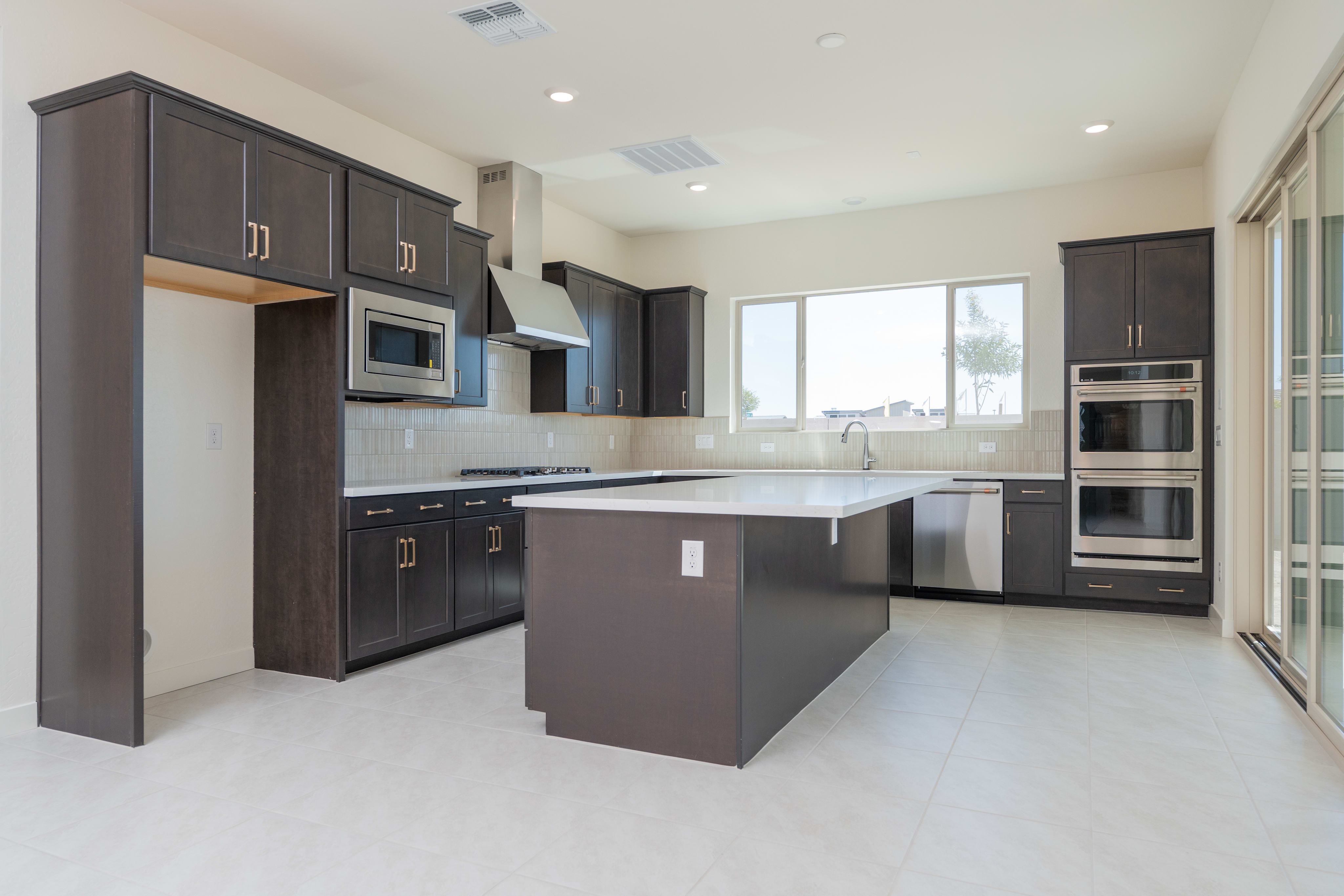 A modern, spacious kitchen with dark-colored cabinets, stainless steel appliances, and a central island with a countertop.