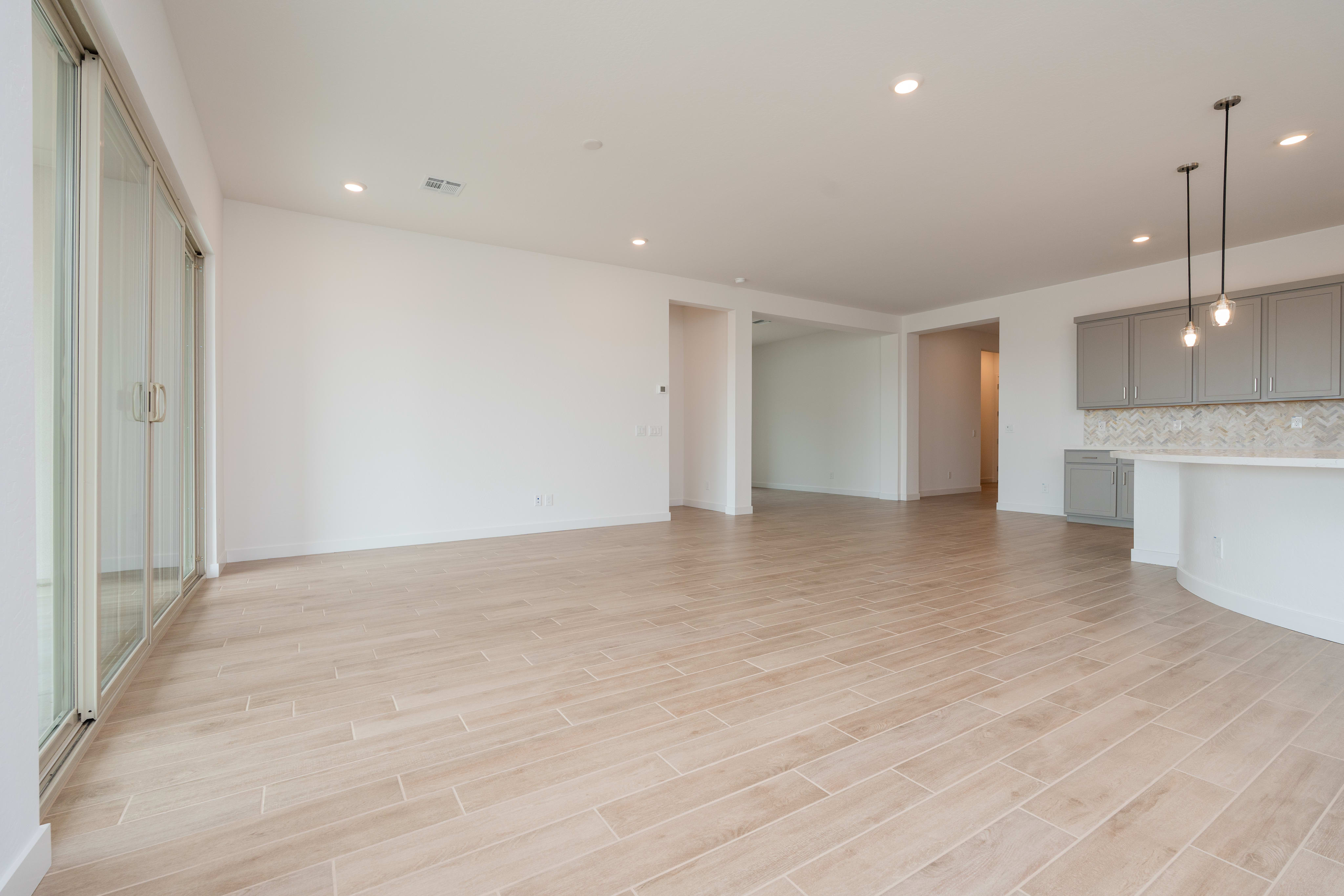 A spacious, open-concept living area with light-colored hardwood floors, white walls, and modern lighting fixtures.