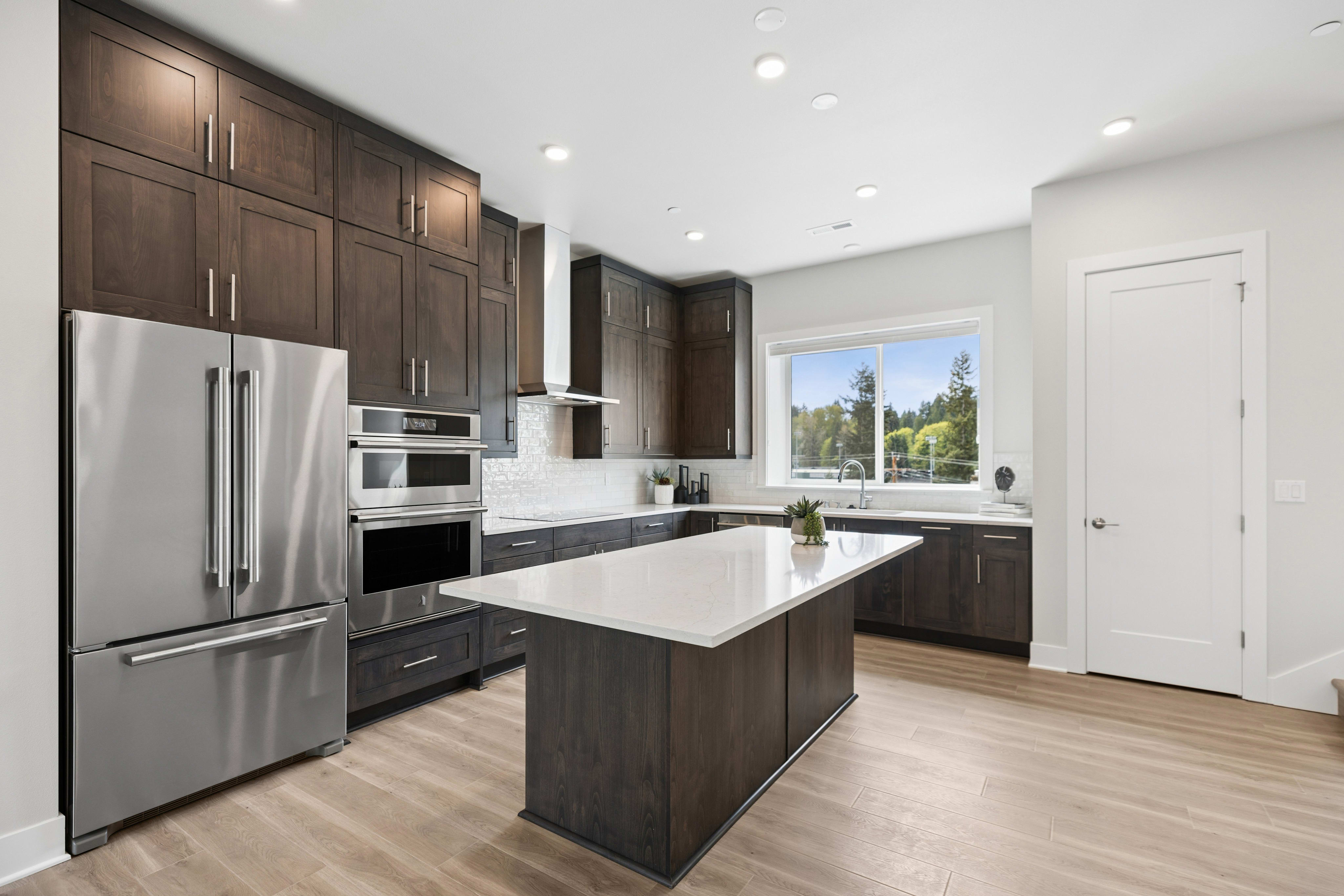 A modern, well-equipped kitchen with dark wood cabinets, stainless steel appliances, and a large window overlooking a scenic outdoor landscape.