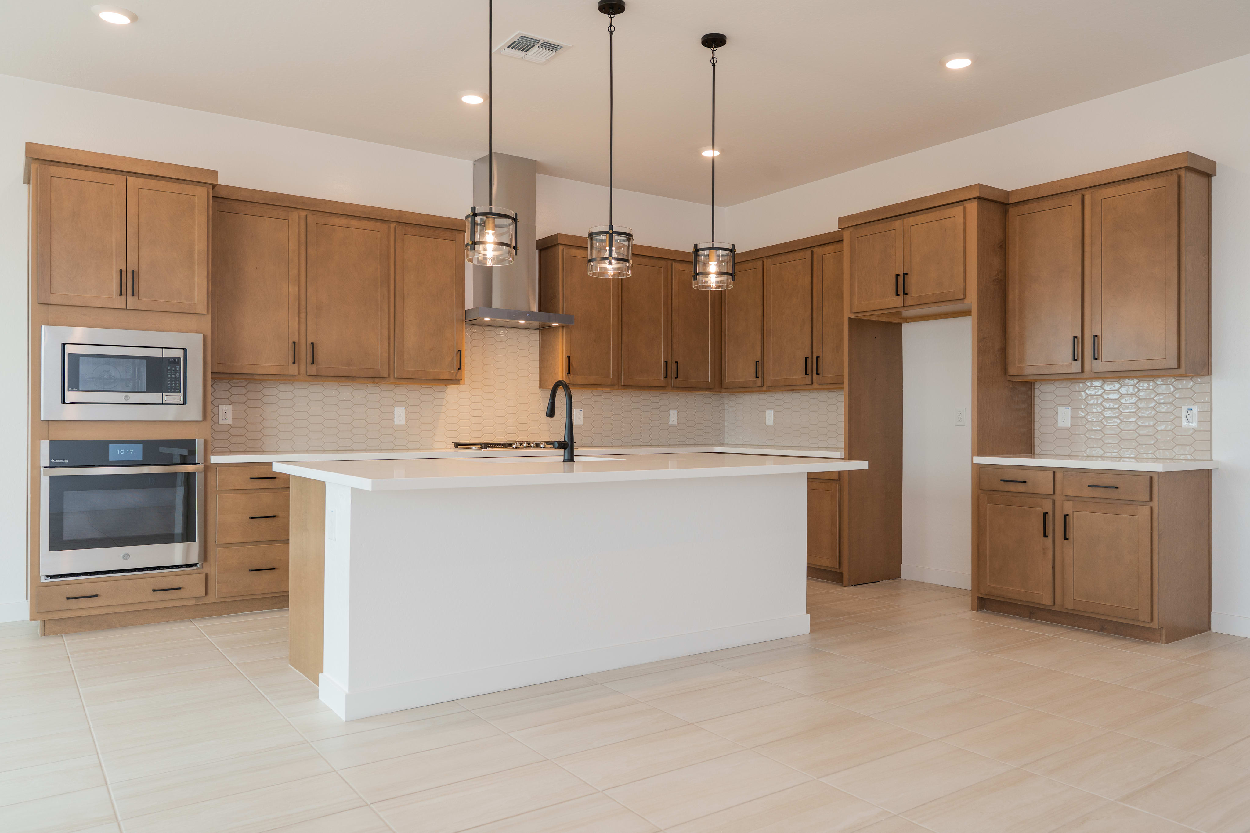 A modern, open-concept kitchen with light wood cabinets, a white island, and pendant lighting fixtures.