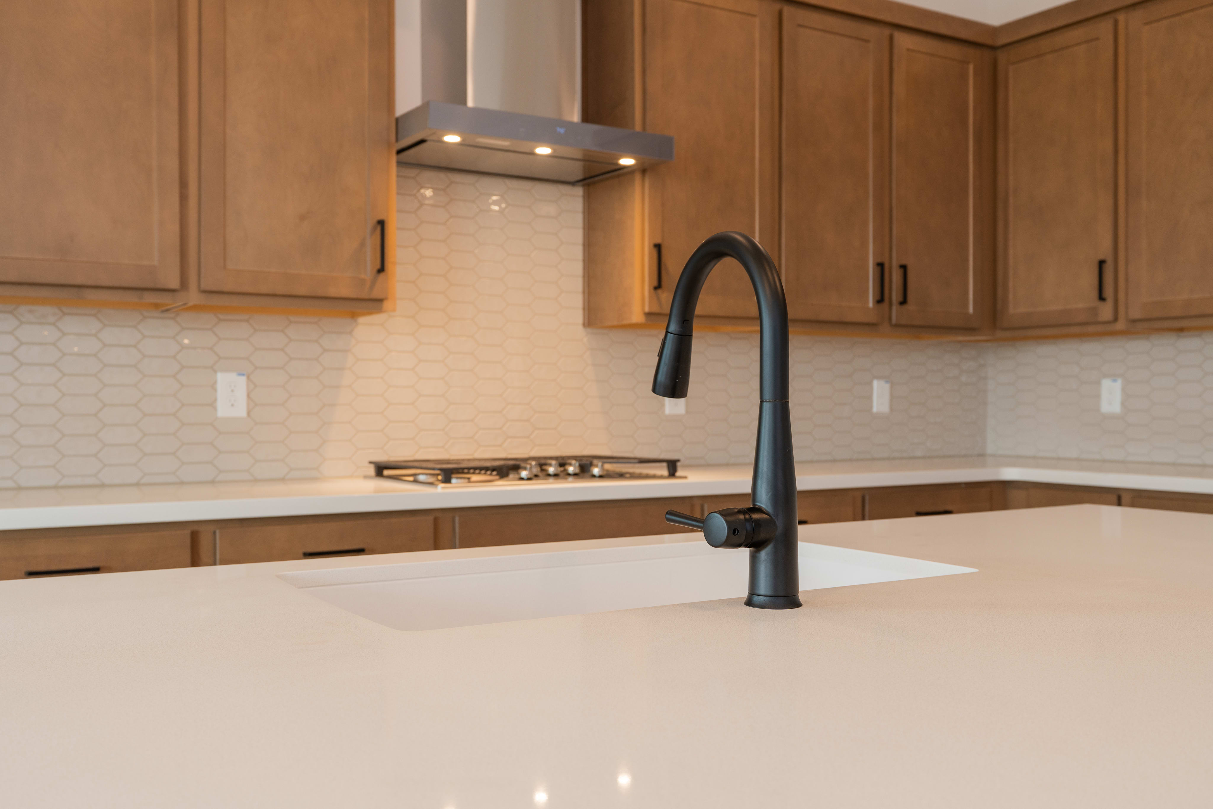 The image shows a modern kitchen with wooden cabinets, a black faucet, and a white countertop.