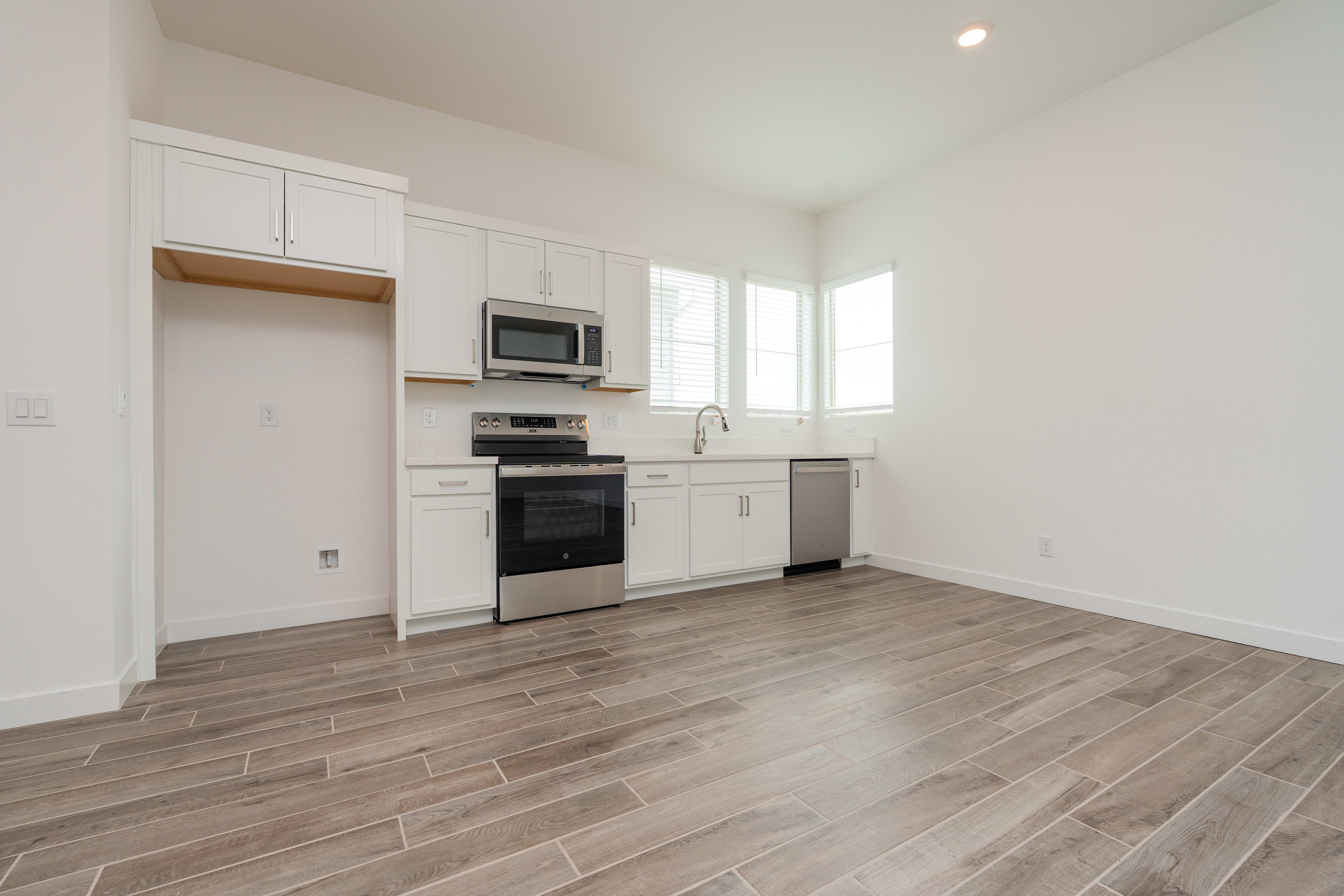 A modern, open-concept kitchen with white cabinets, stainless steel appliances, and a hardwood-style tile floor, set against a bright, airy background.