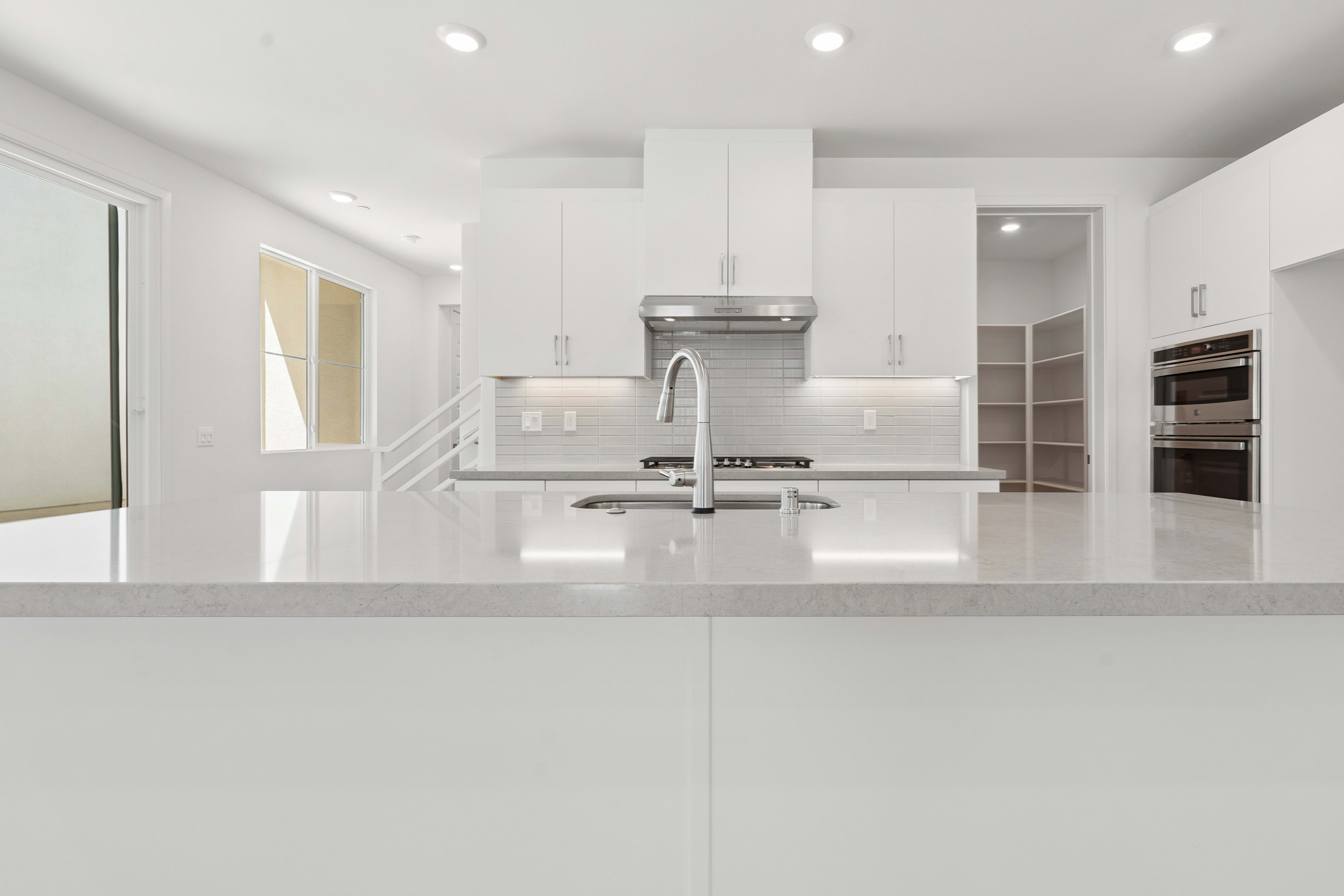 A modern, minimalist kitchen with sleek white cabinets, stainless steel appliances, and a large central island with a smooth countertop.