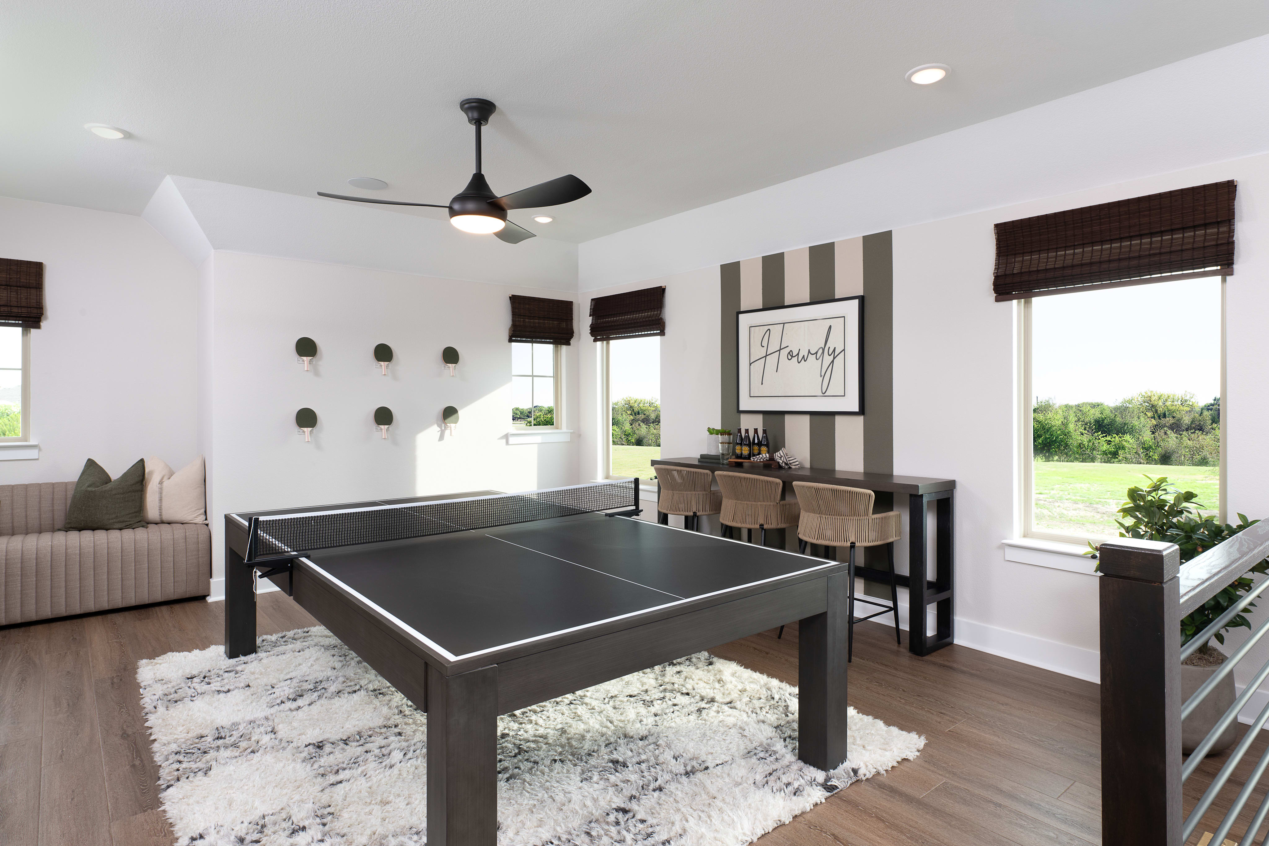 A modern and stylish game room with a ping-pong table, comfortable seating, and large windows overlooking a scenic outdoor landscape.