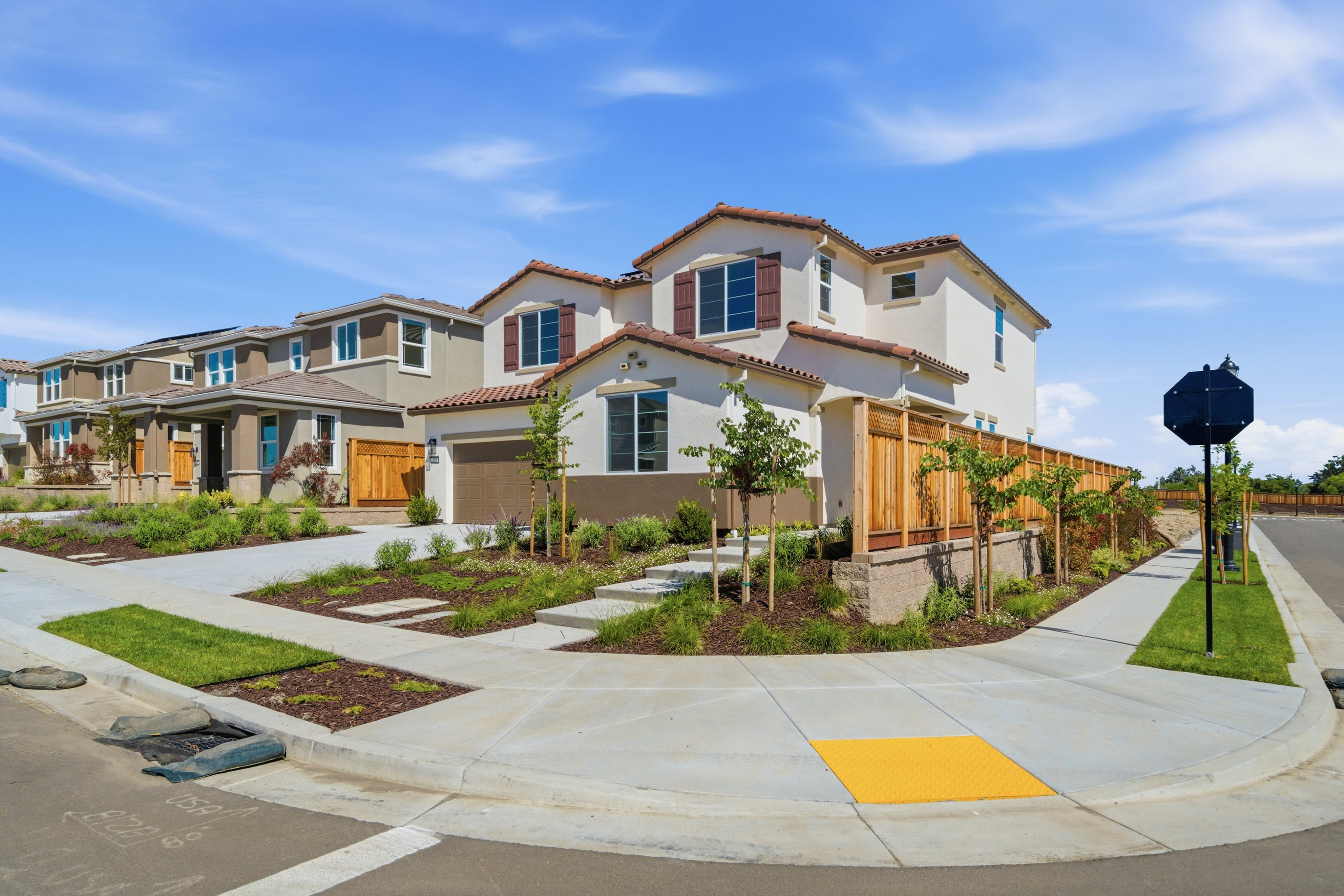 A residential neighborhood with multiple two-story houses, landscaped yards, and a paved walkway in the foreground.
