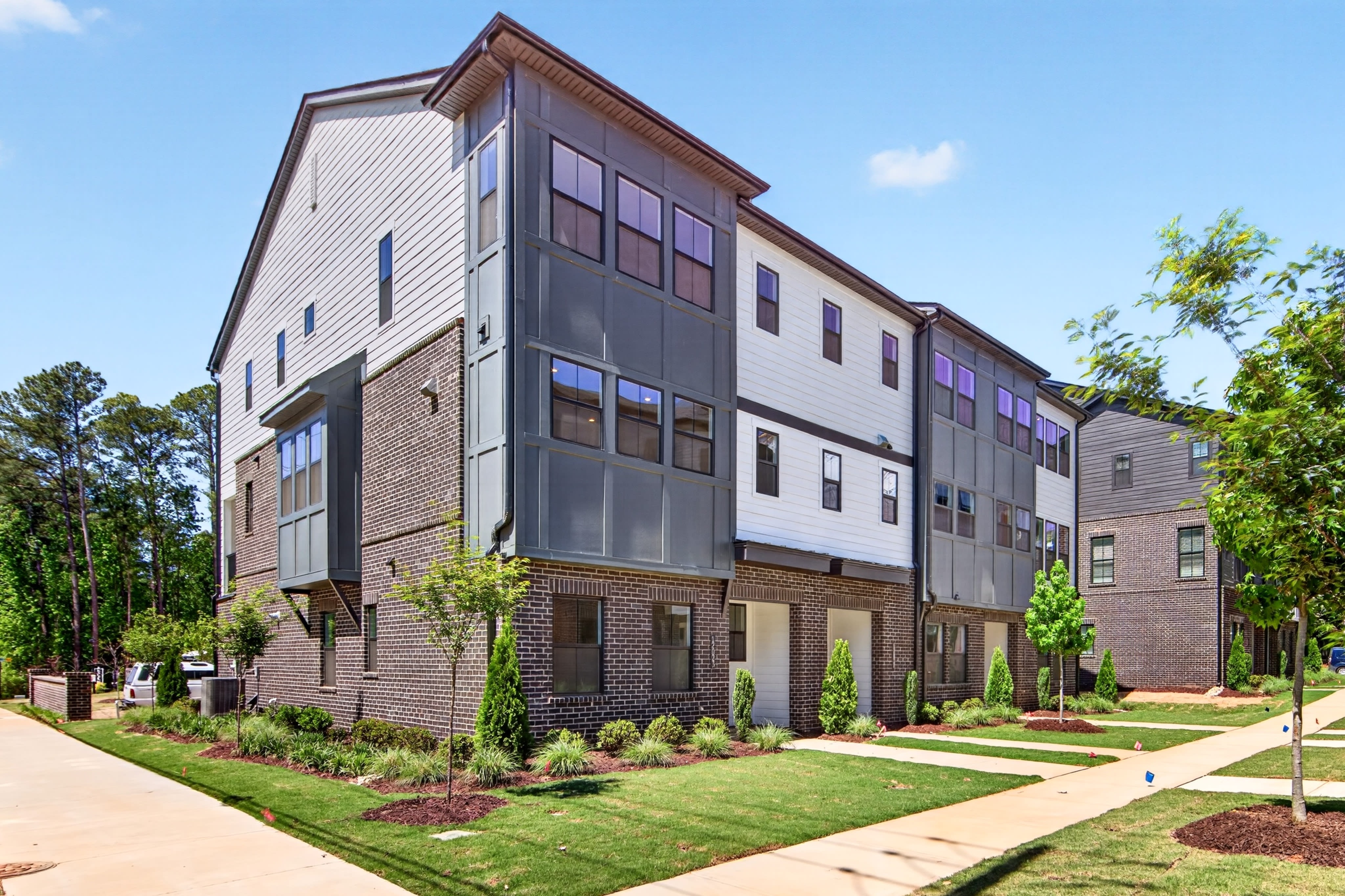 A multi-story residential building with a brick and siding exterior, surrounded by a well-manicured lawn and landscaping, set against a backdrop of trees and a clear blue sky.