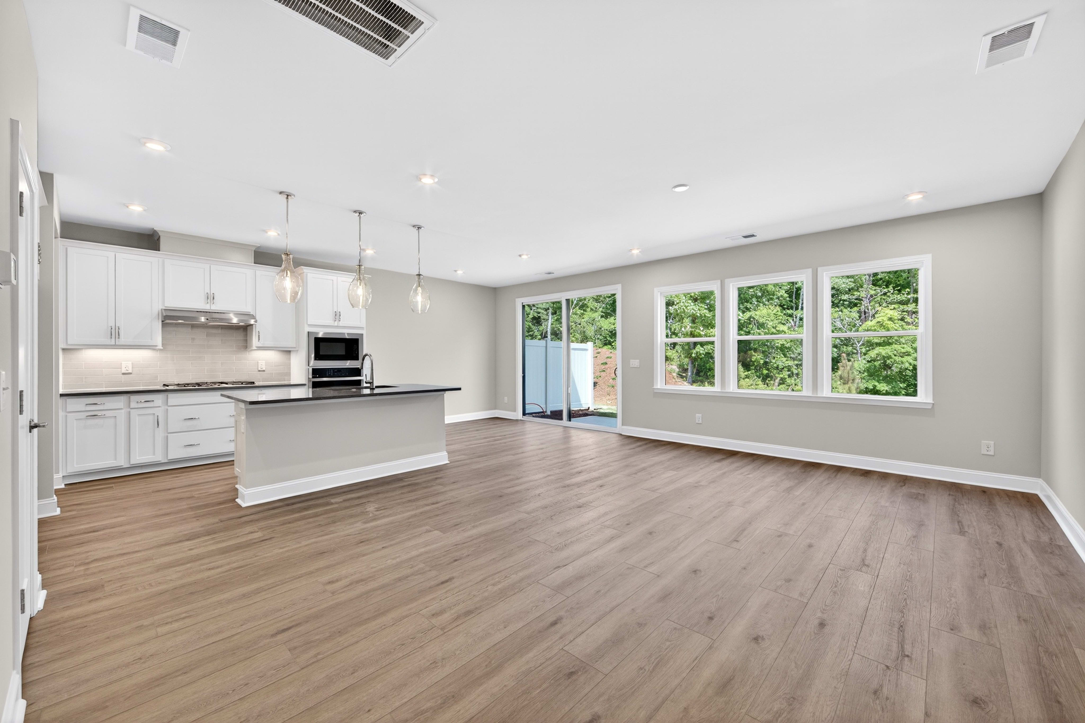 A modern, open-concept living space with a sleek kitchen in the foreground and large windows overlooking a lush green background.