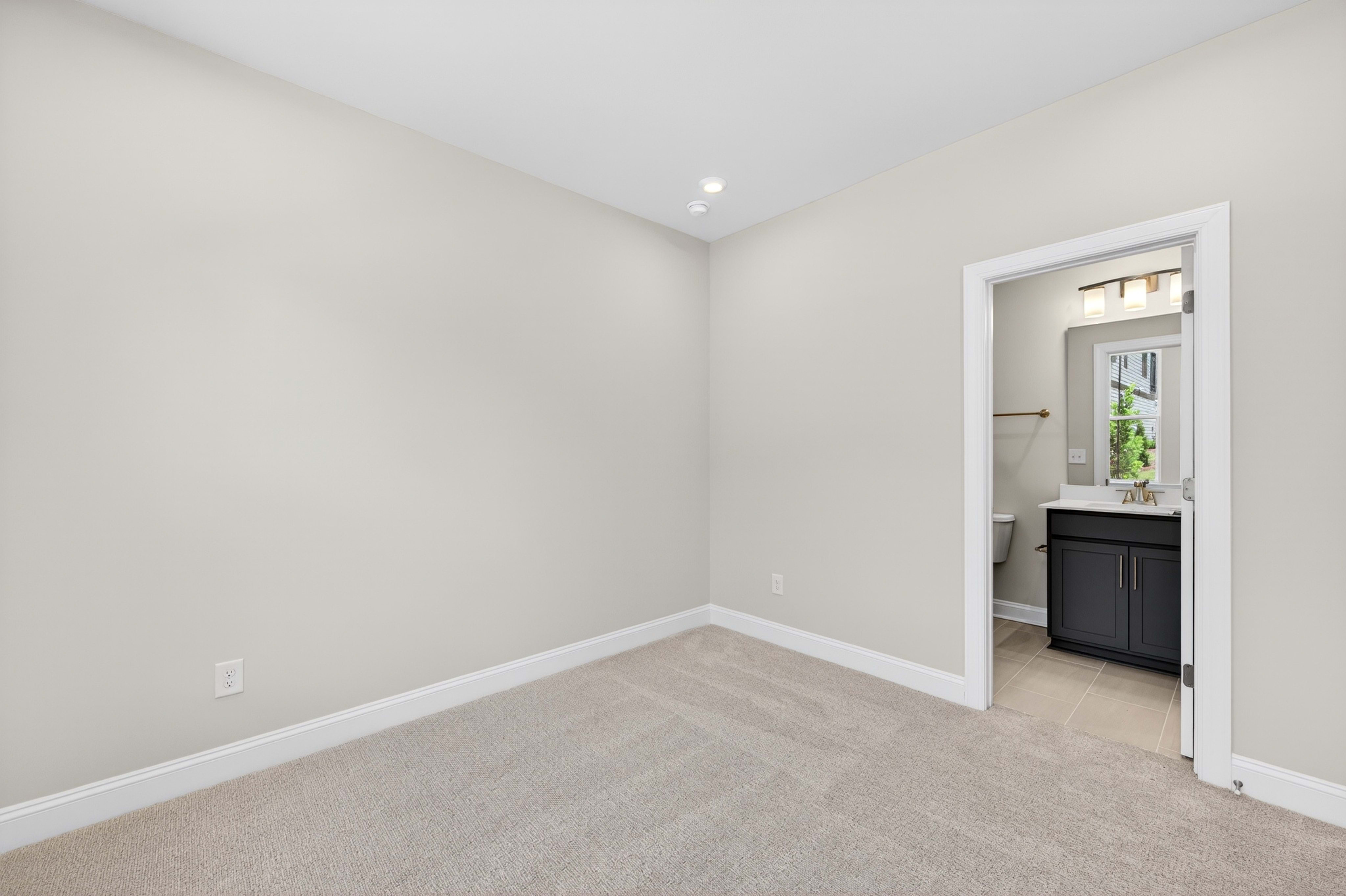 A carpeted room with a doorway opening to a bathroom with a vanity and toilet.