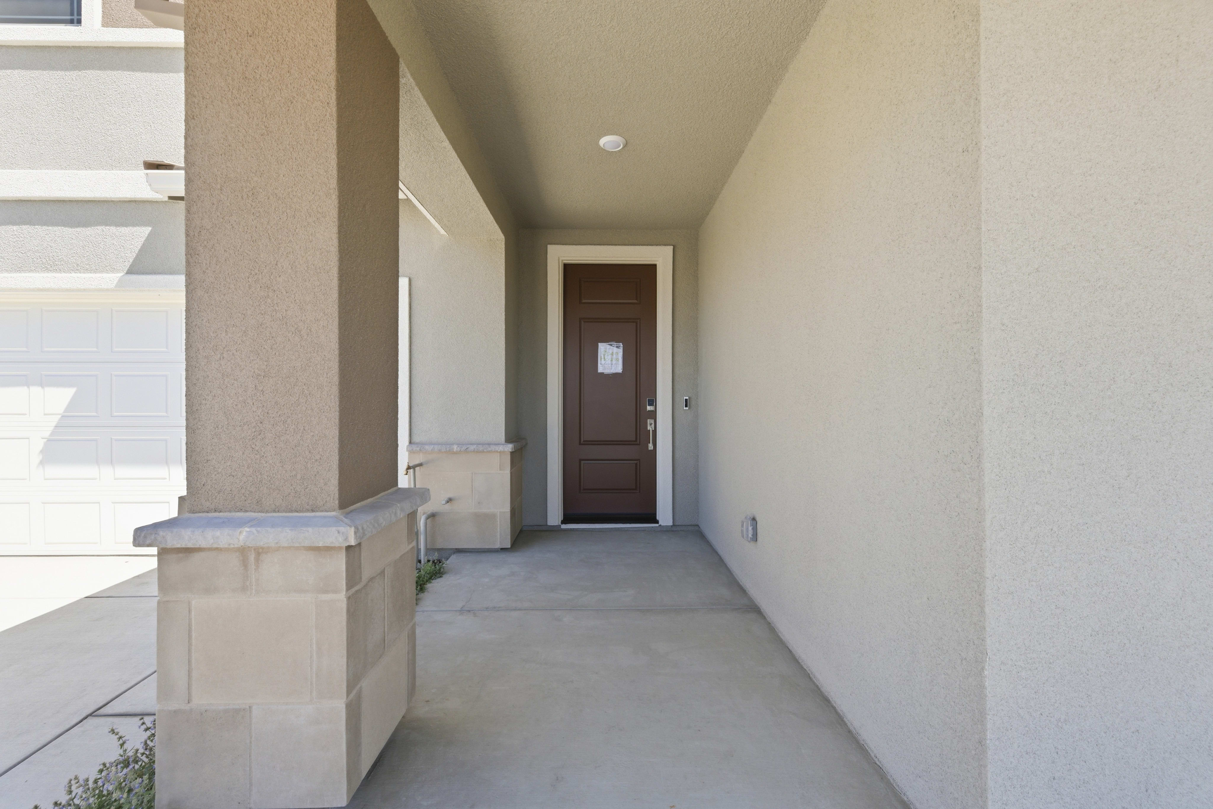 A concrete walkway leads to a brown front door, with a beige stucco house and garage visible in the background.