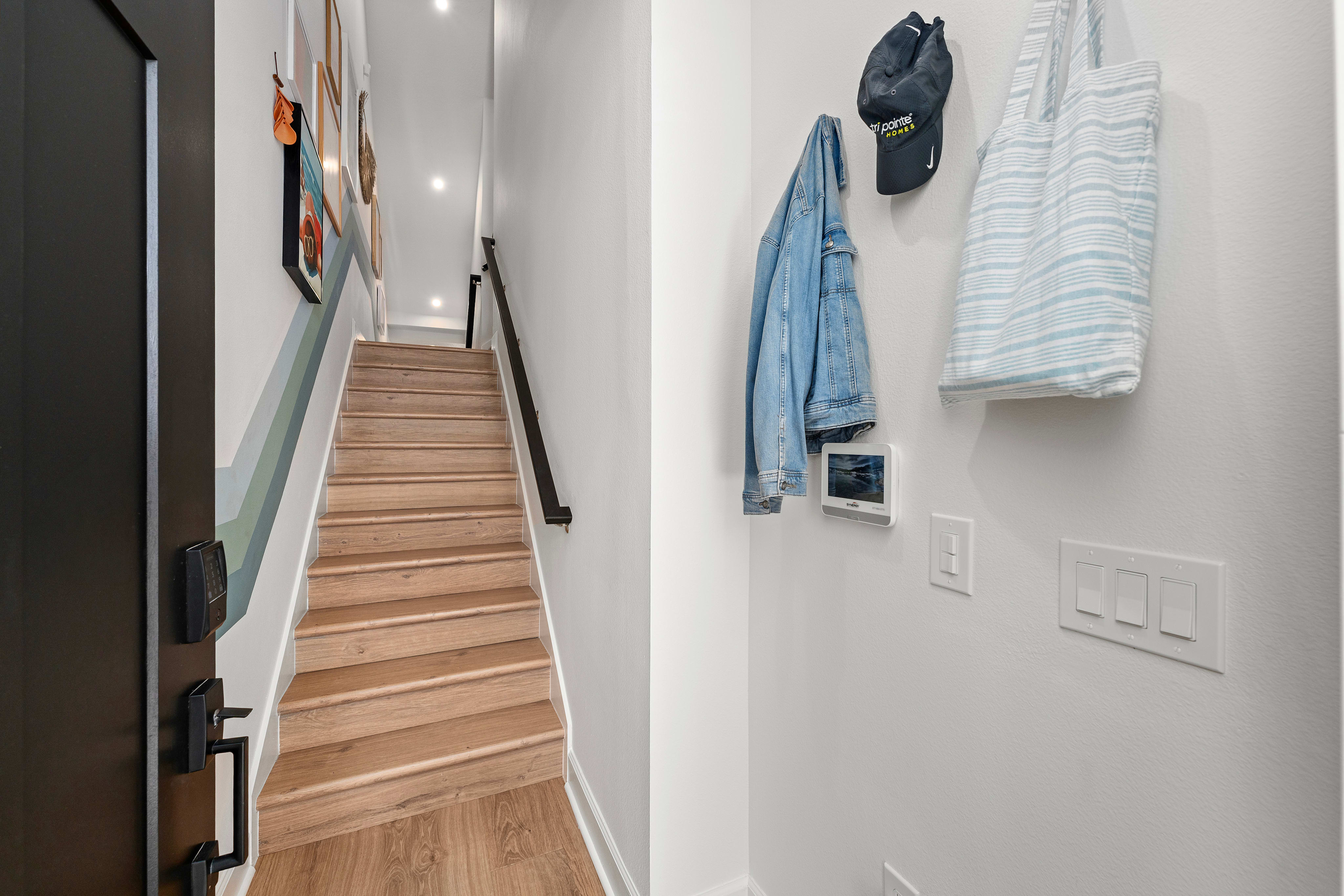 A wooden staircase with a colorful stripe ascends to the background, while a denim jacket, a hat, and a tote bag hang on the wall in the foreground.