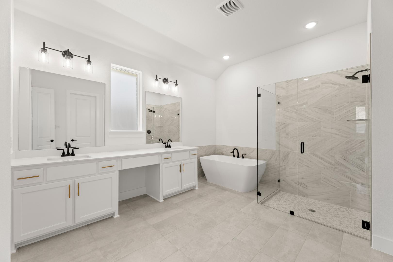 A modern white bathroom features a double vanity in the foreground and a freestanding tub and glass-enclosed shower in the background.