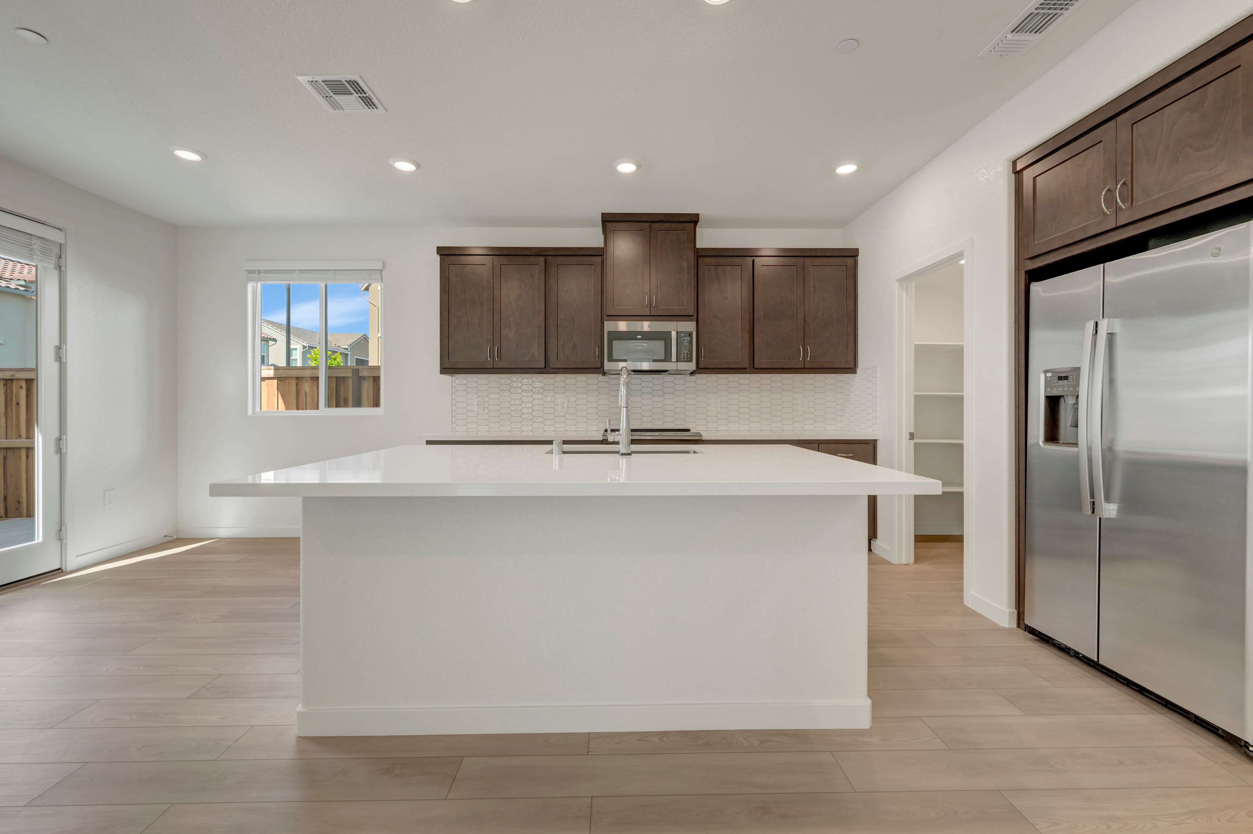 A modern kitchen with a white island in the foreground and dark wood cabinets and stainless steel appliances in the background.