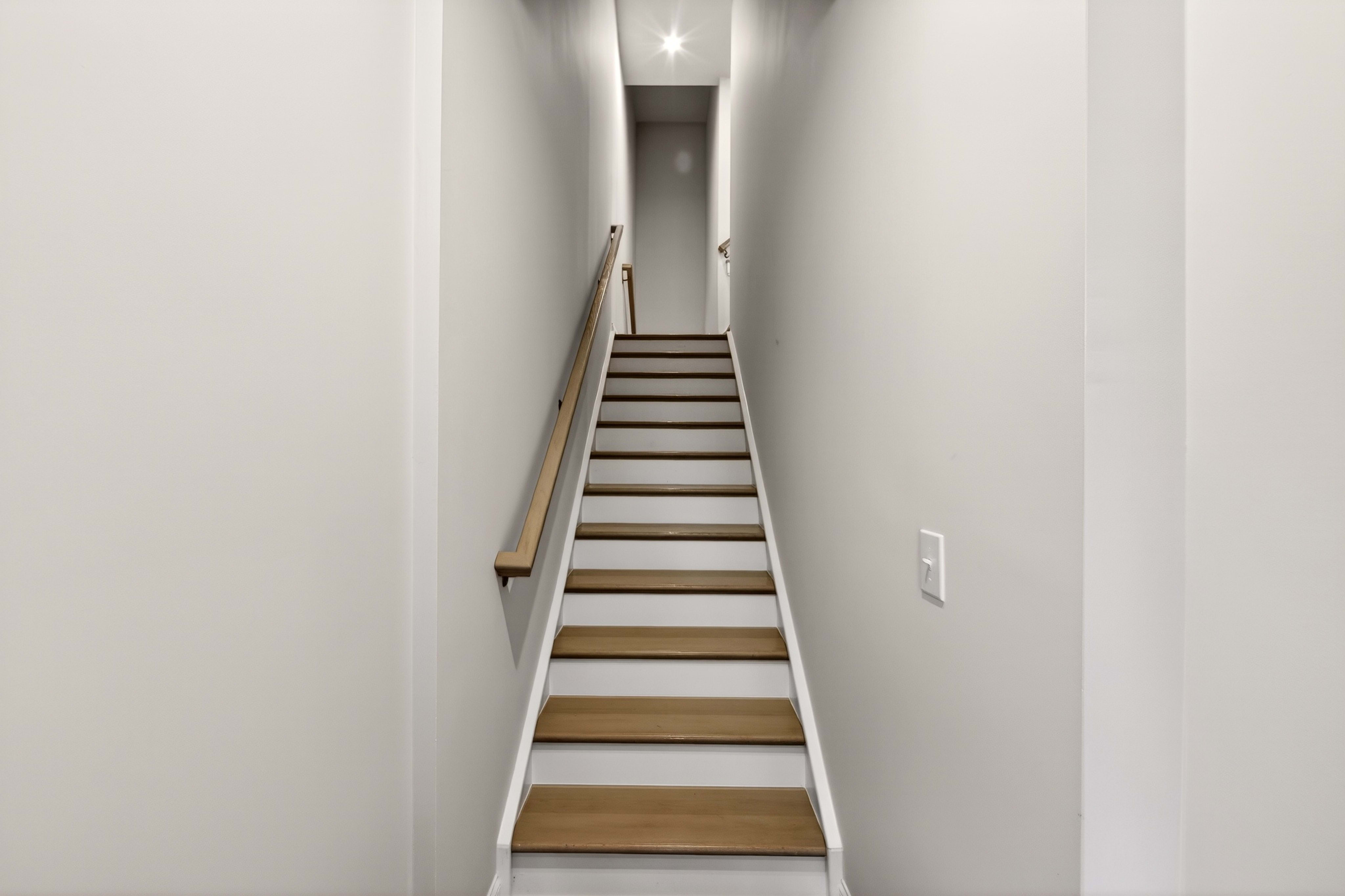 A narrow staircase with light wood treads and white risers ascends into a dimly lit hallway.