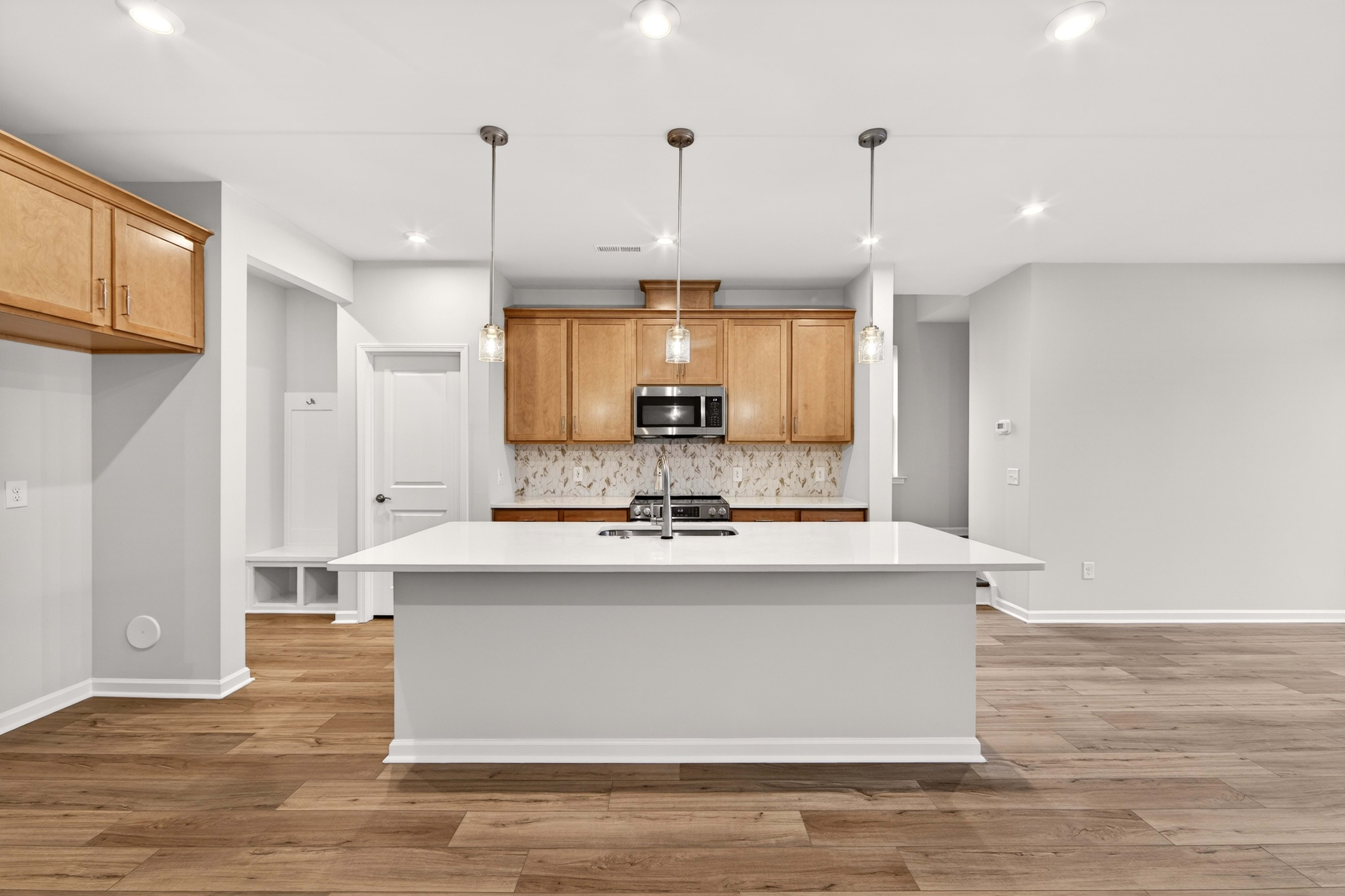 A modern kitchen with a white island in the foreground and light wood cabinets and appliances in the background.