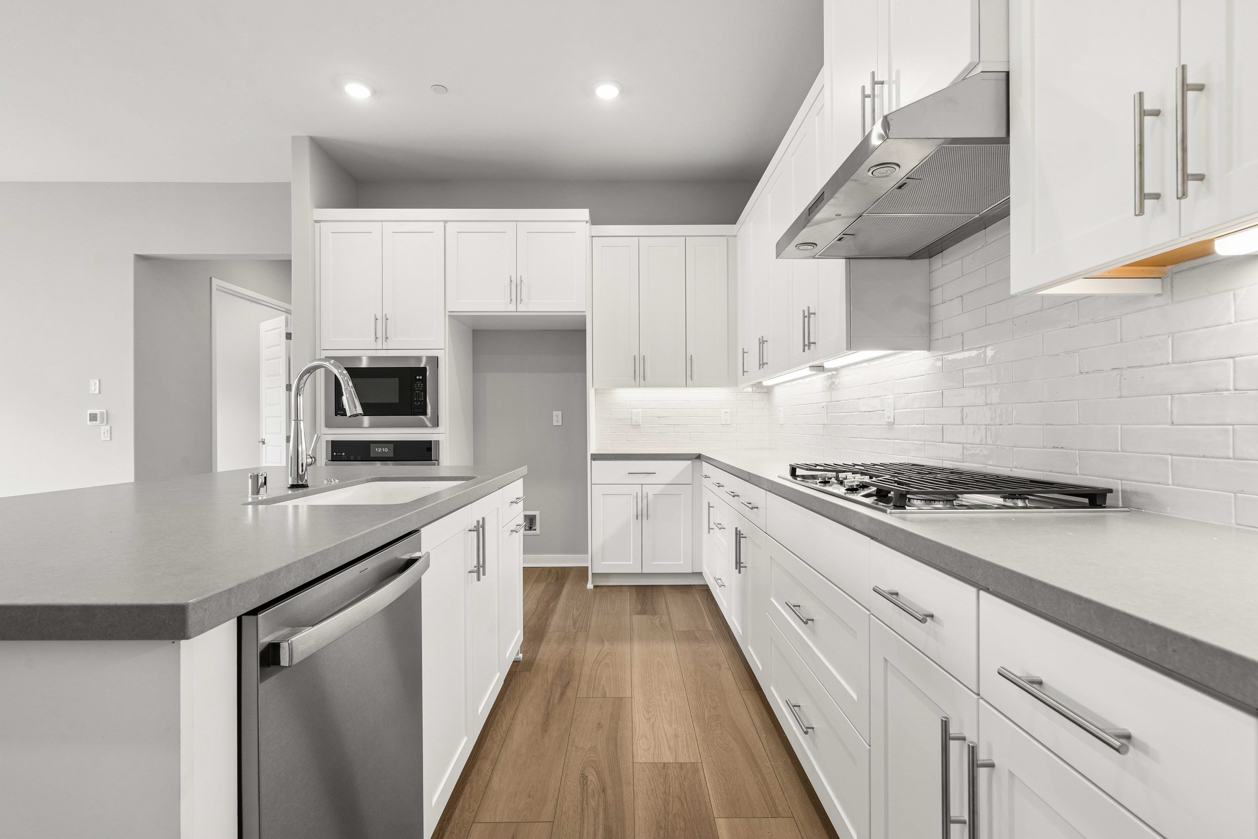 A modern white kitchen with a gray island in the foreground and white cabinets and appliances in the background.