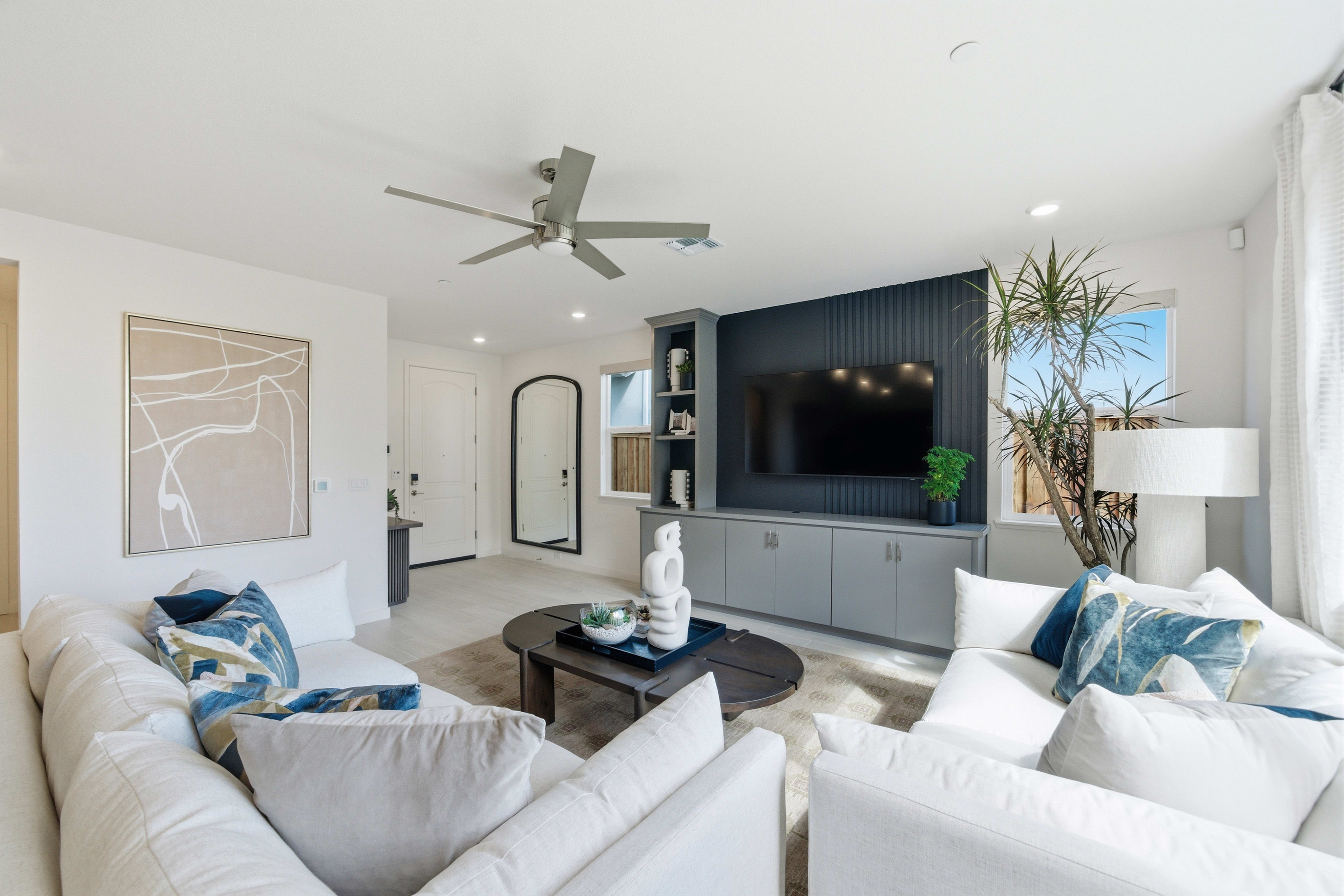 A modern living room with plush white sofas in the foreground and a sleek entertainment center with a large television in the background.