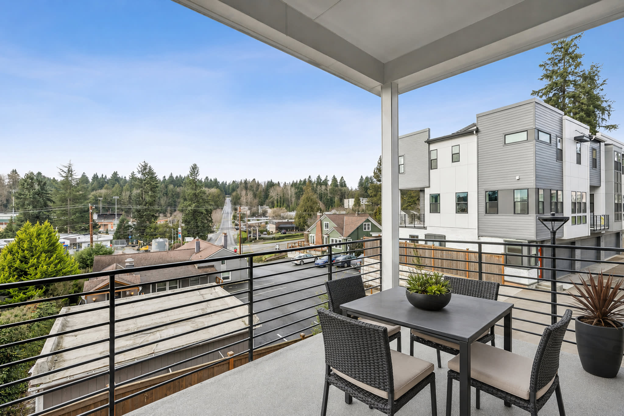 A patio with a table and chairs overlooks a suburban neighborhood with modern townhouses in the background.