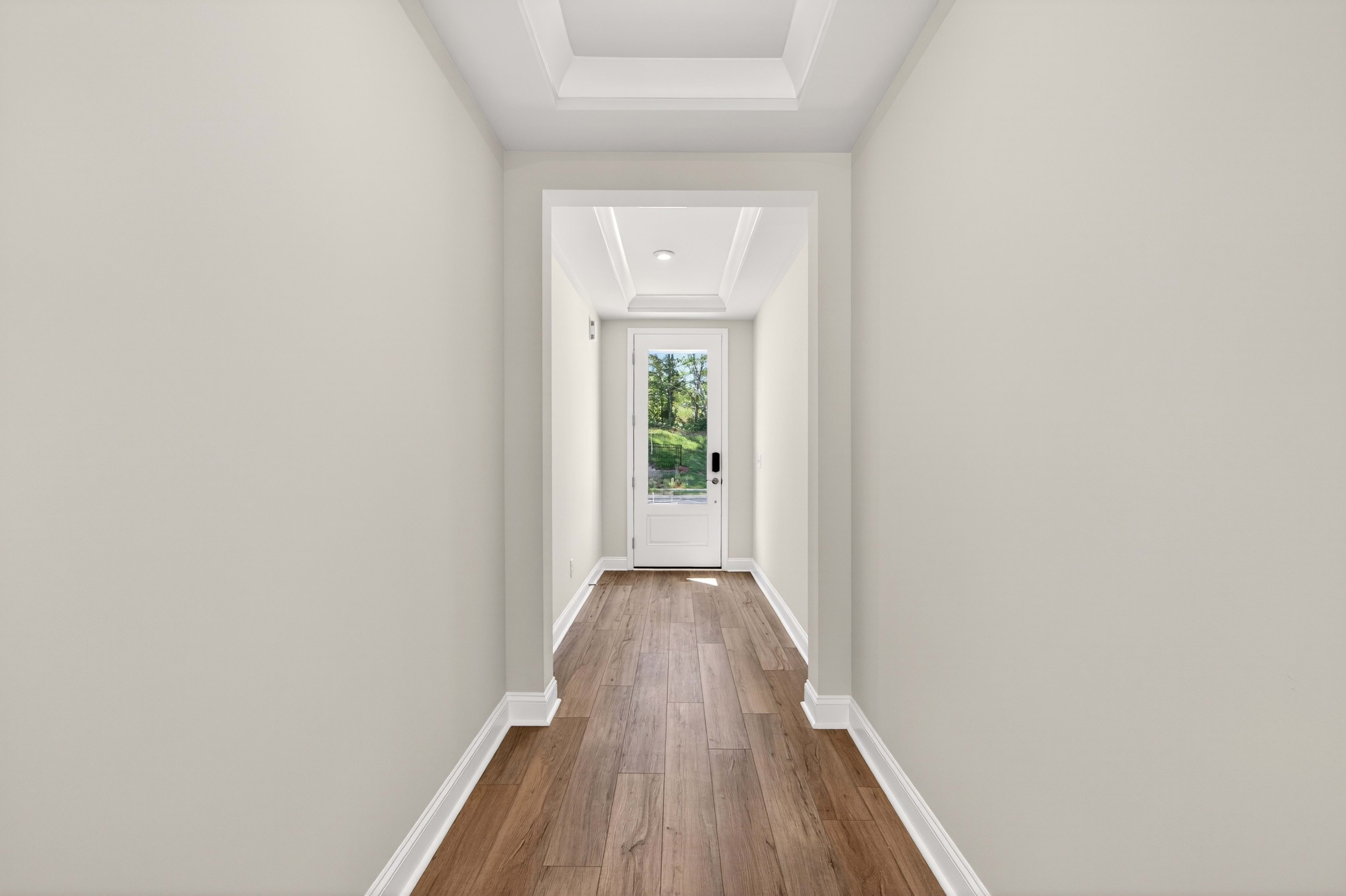 A wooden floor hallway leads to a glass door with greenery visible outside.