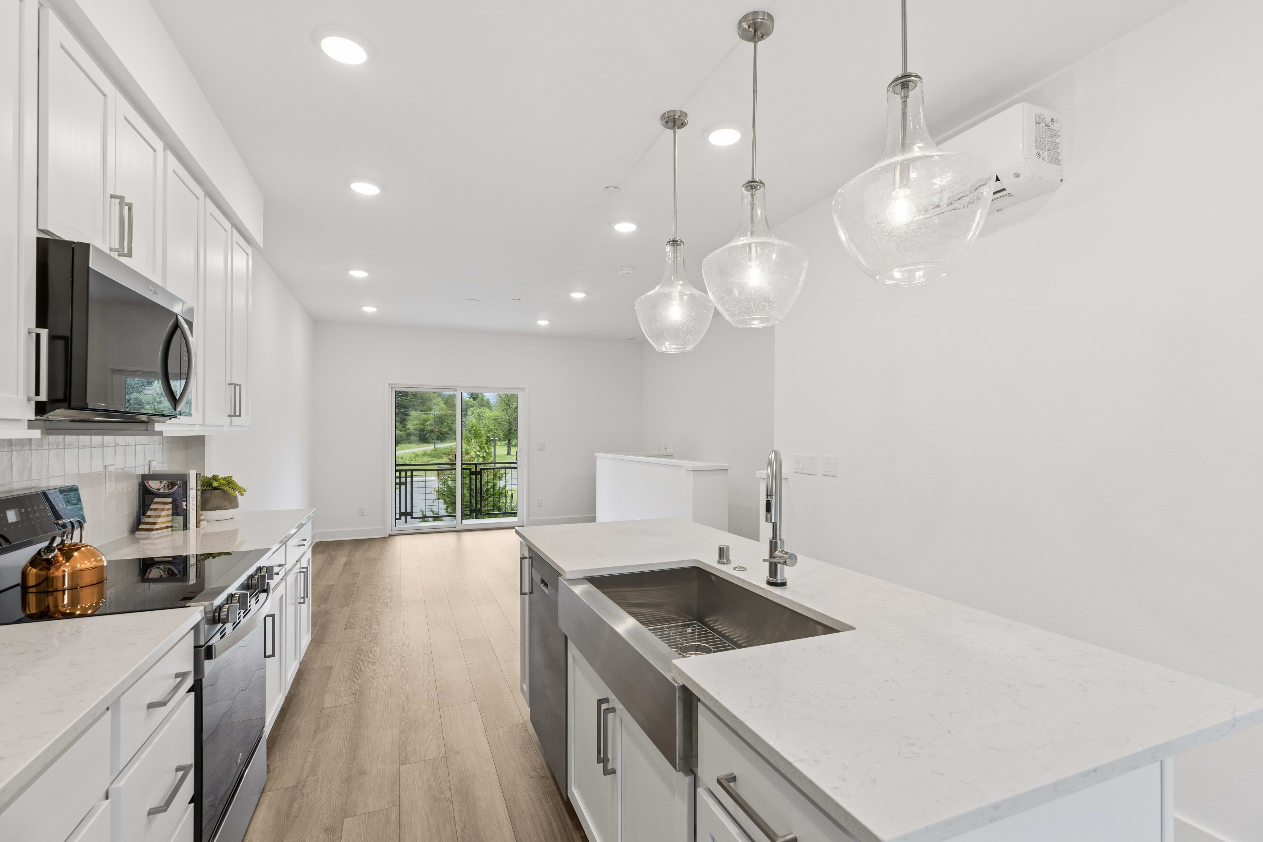 A modern kitchen island with a farmhouse sink is in the foreground, while a living area with a view of a lake is in the background.