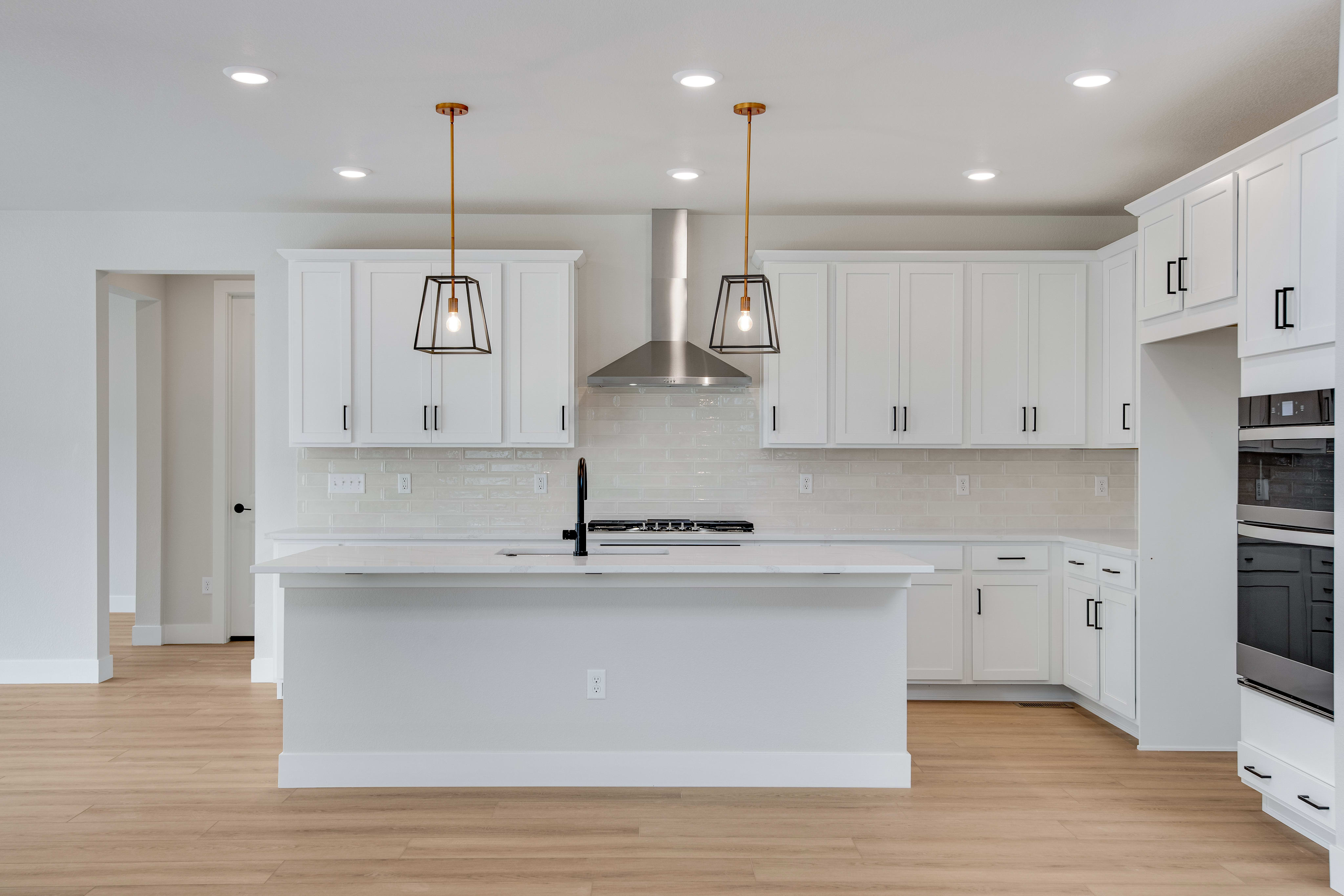 A modern white kitchen with a central island in the foreground and white cabinets and appliances in the background.