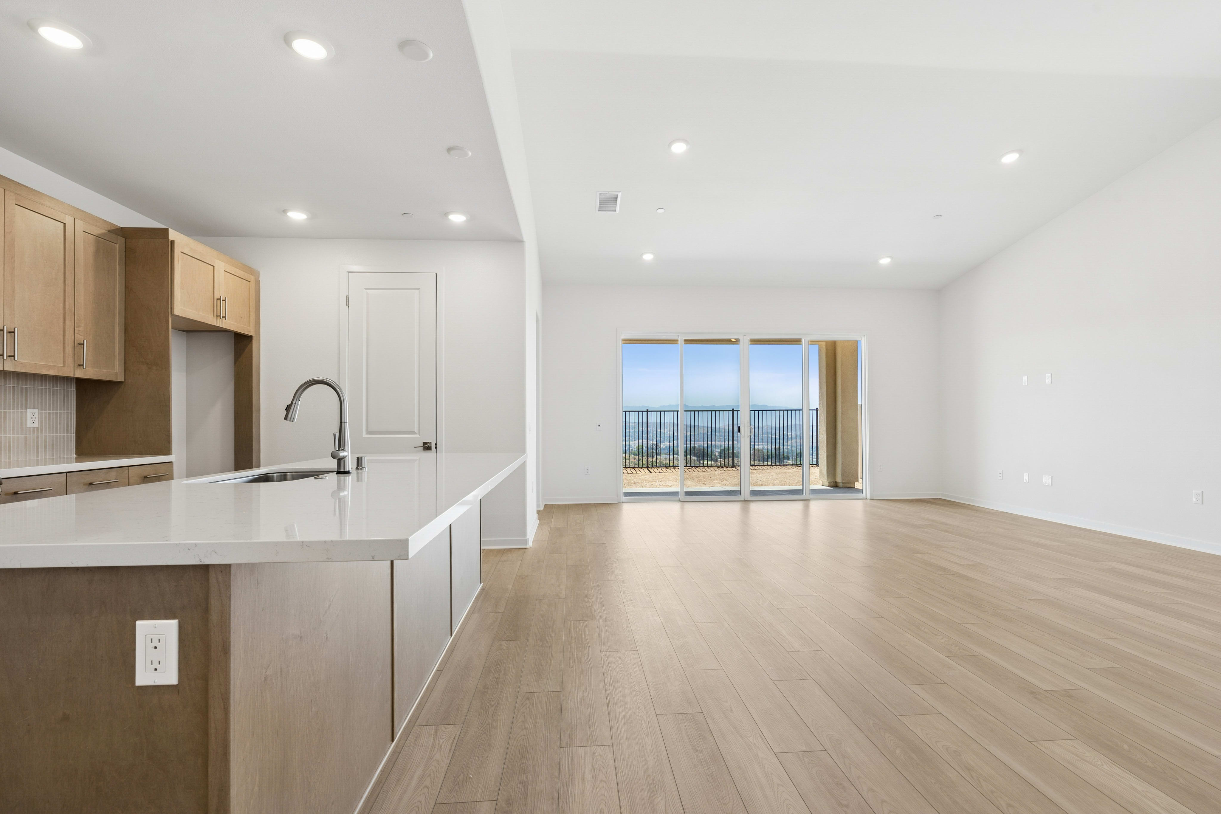 A modern kitchen island with a sink is in the foreground, while a spacious living area with large sliding glass doors offering a scenic view of the ocean is in the background.