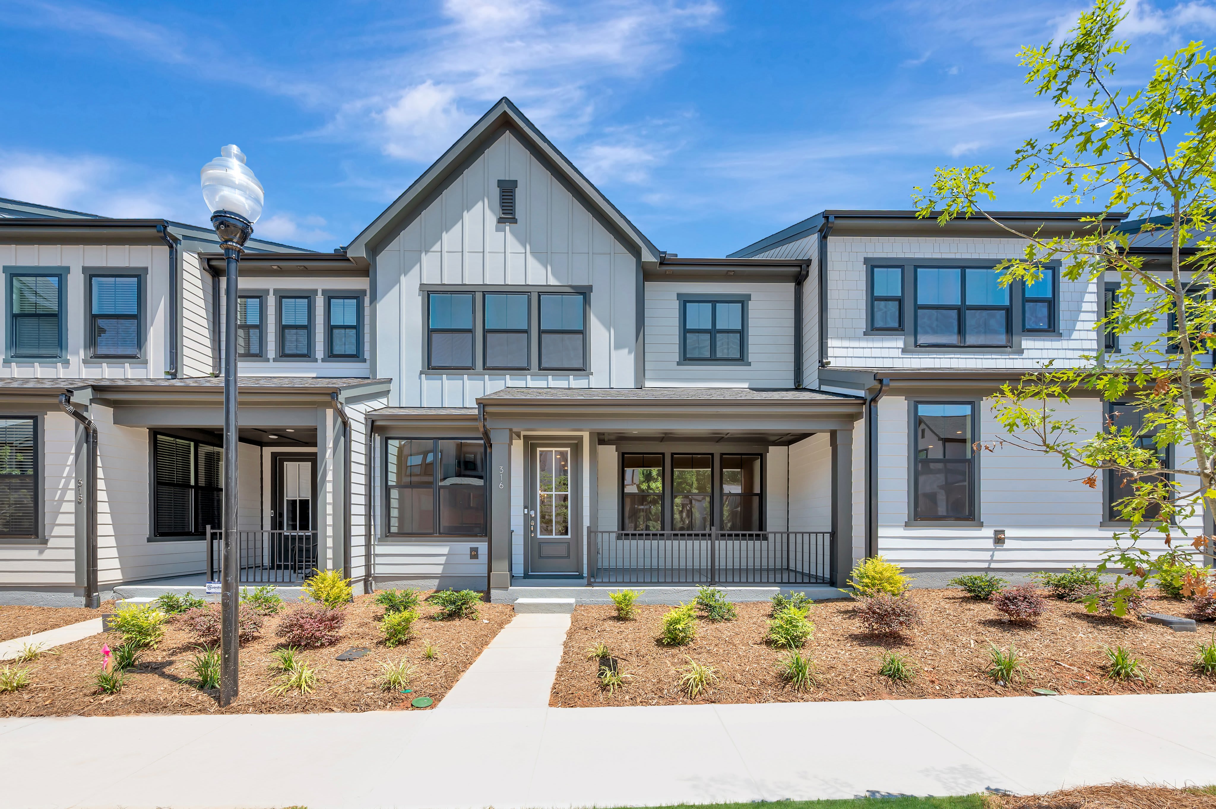 A modern townhouse with a covered porch and manicured landscaping sits under a bright blue sky.