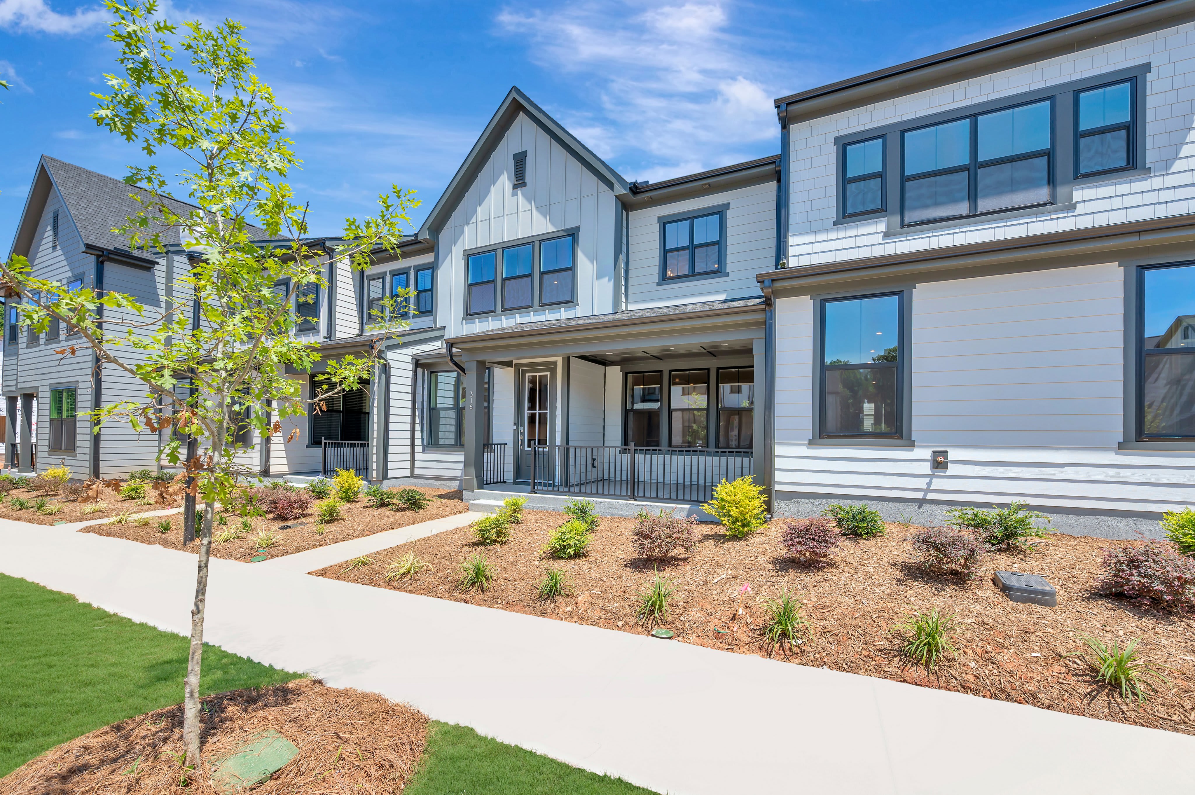 A modern townhouse complex with manicured landscaping in the foreground and a clear blue sky in the background.