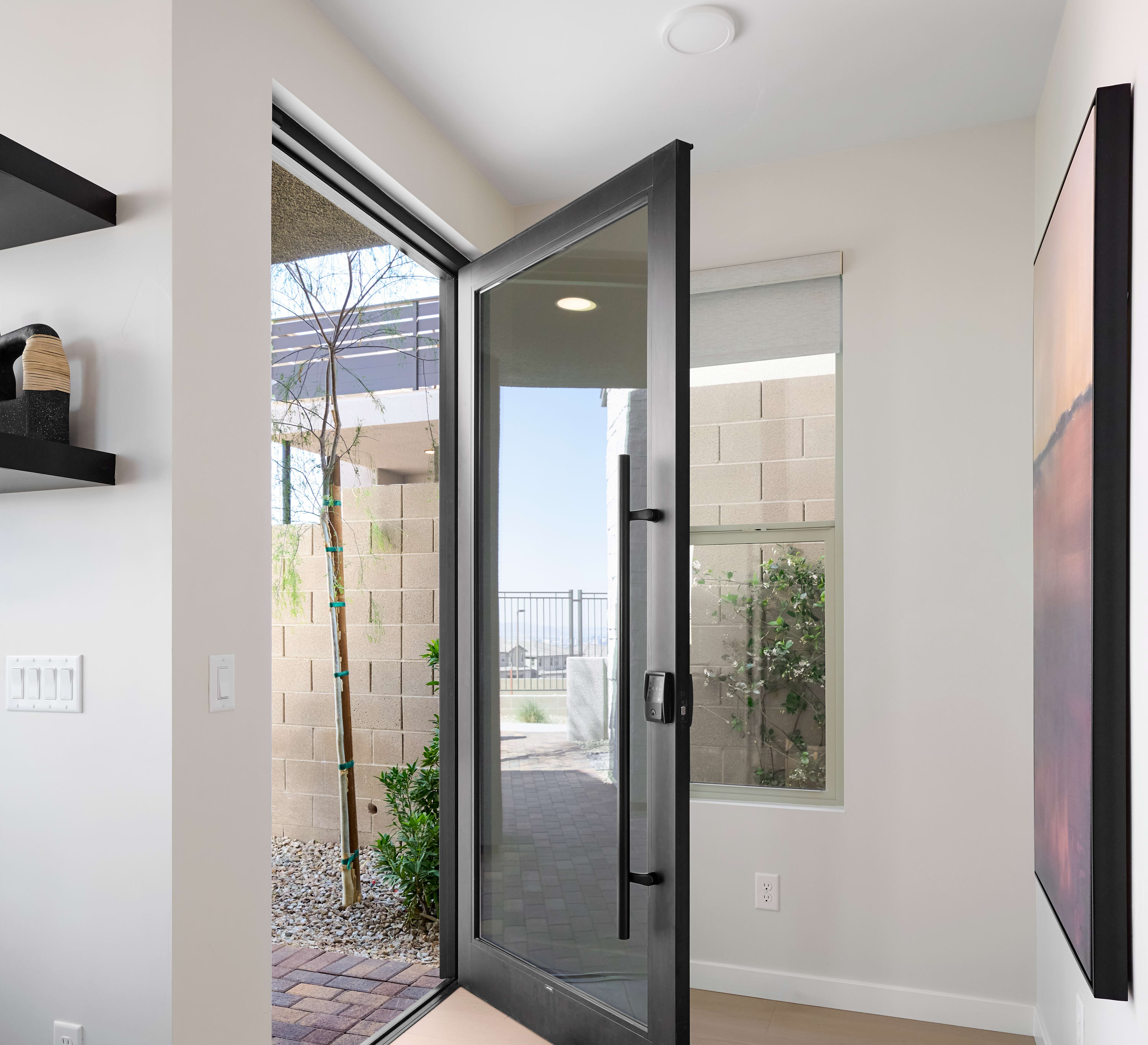A modern entryway with a large pivot door opening to a courtyard, and a contemporary painting on the wall.