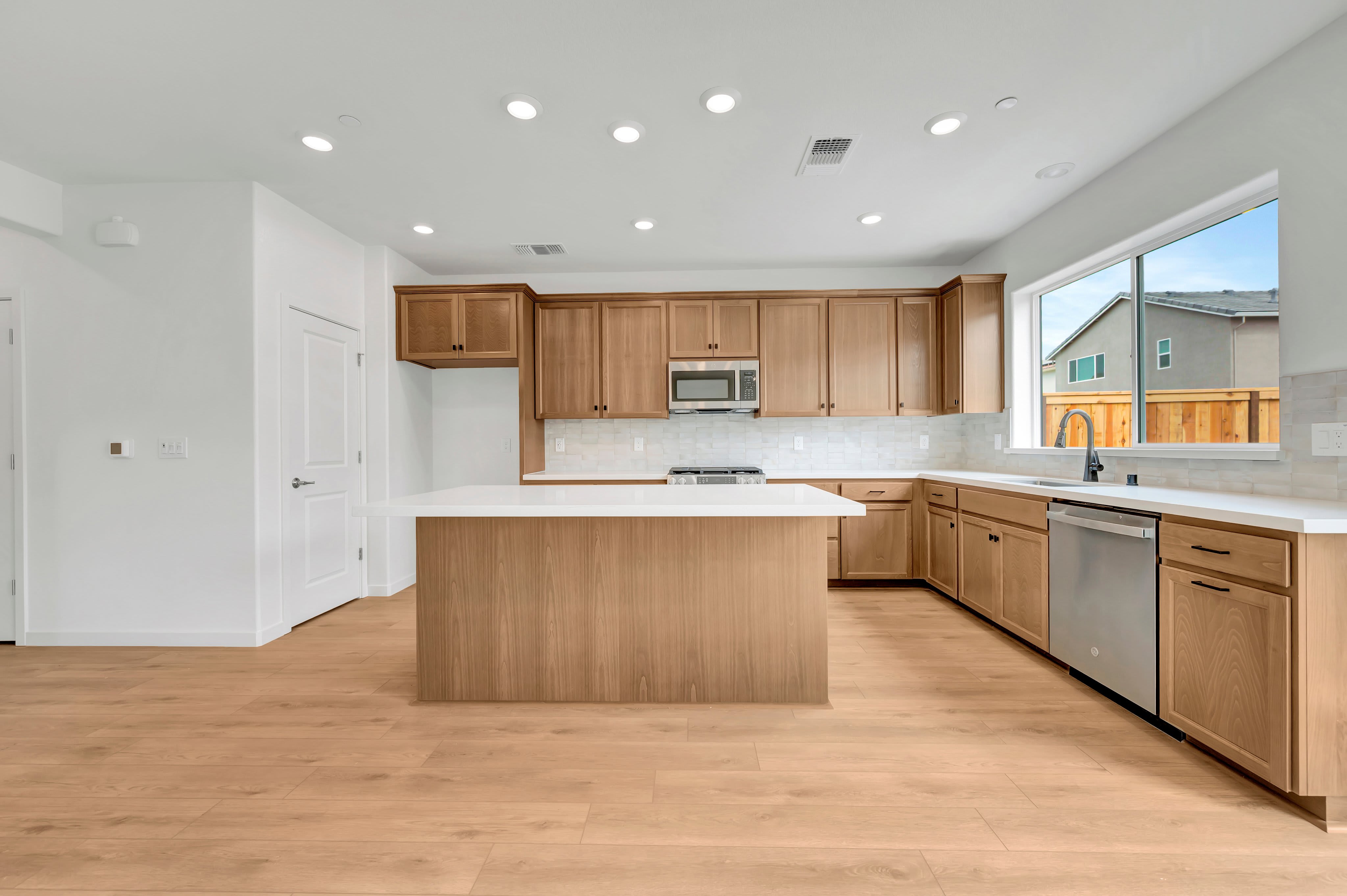 A modern kitchen with a light wood island in the foreground and a large window overlooking houses in the background.