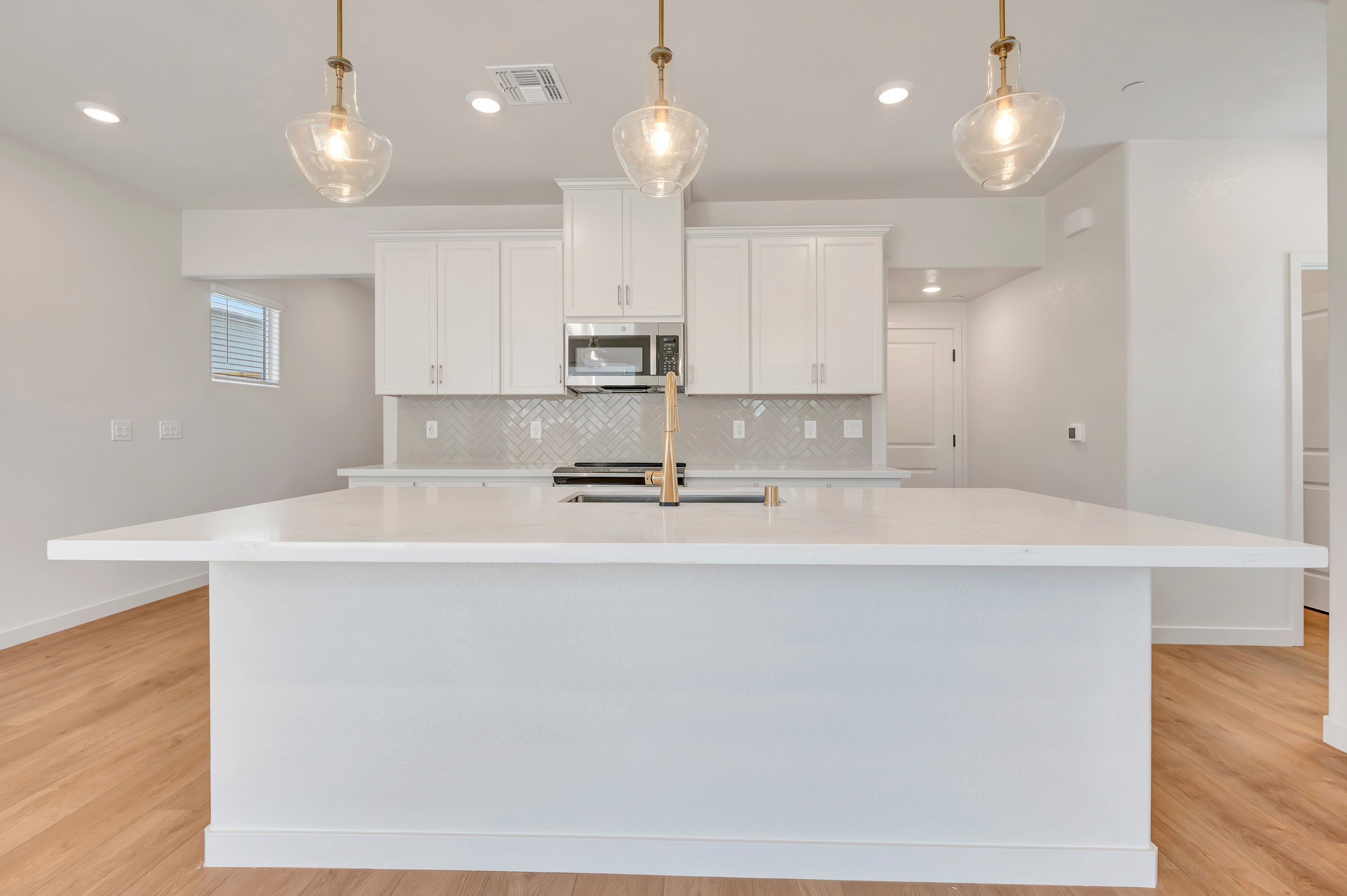 A modern white kitchen island with a waterfall countertop dominates the foreground, while the background features white cabinetry, stainless steel appliances, and pendant lighting.