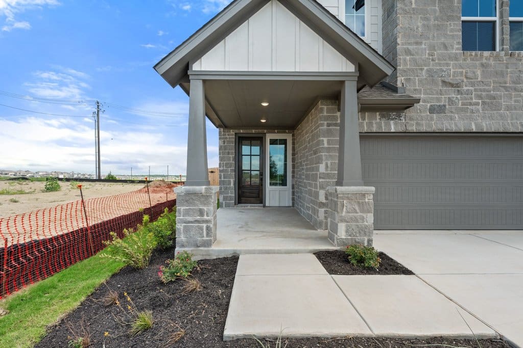 A modern stone-clad house with a covered porch and a clear blue sky in the background.