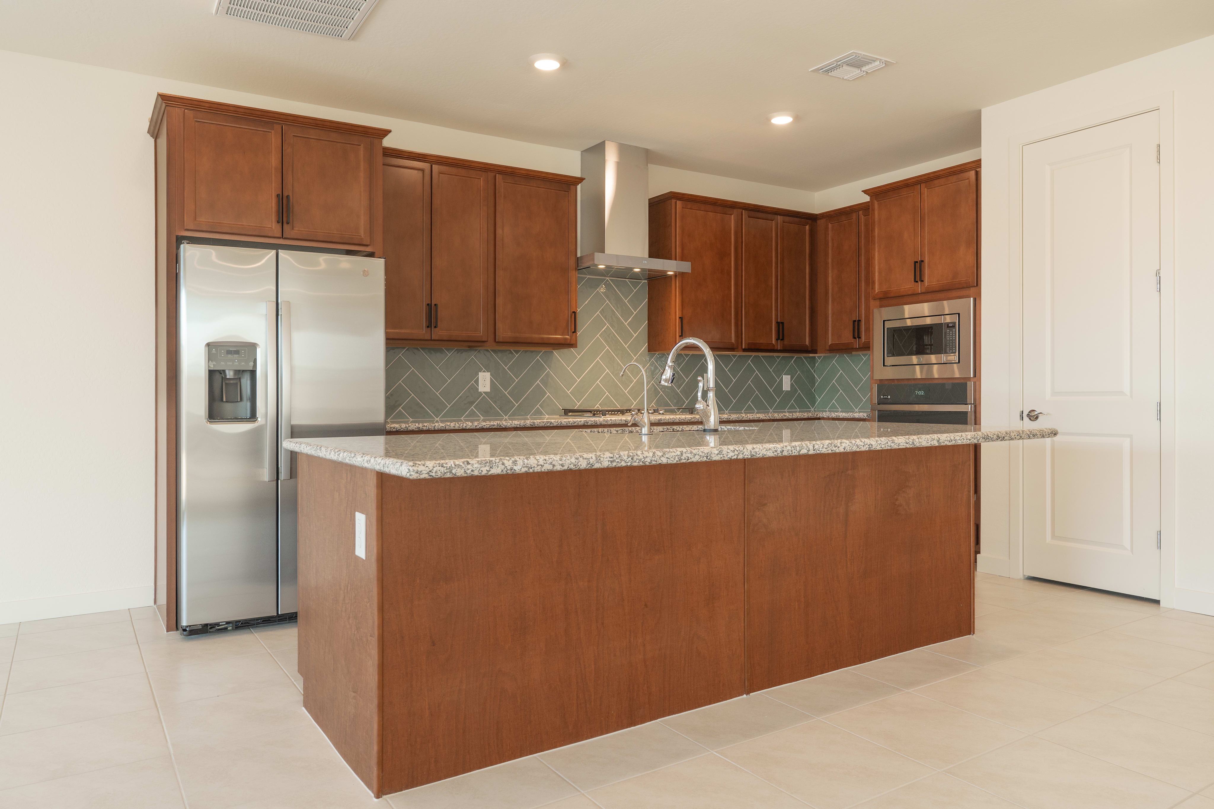 A modern kitchen features a large wooden island in the foreground, with stainless steel appliances and cabinetry filling the background.
