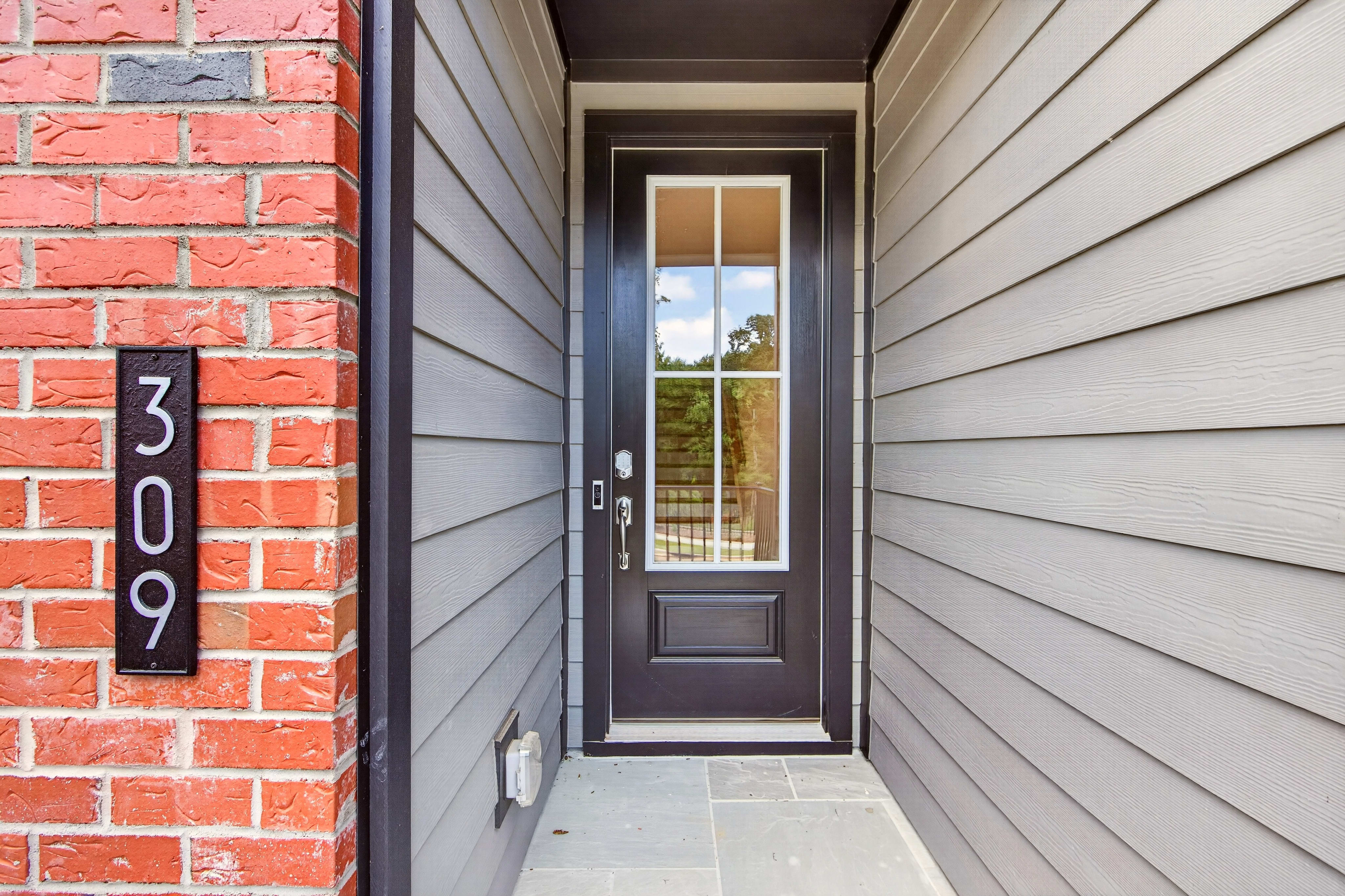 A dark front door with a glass pane is flanked by red brick and gray siding, with the house number 309 visible on the brick.