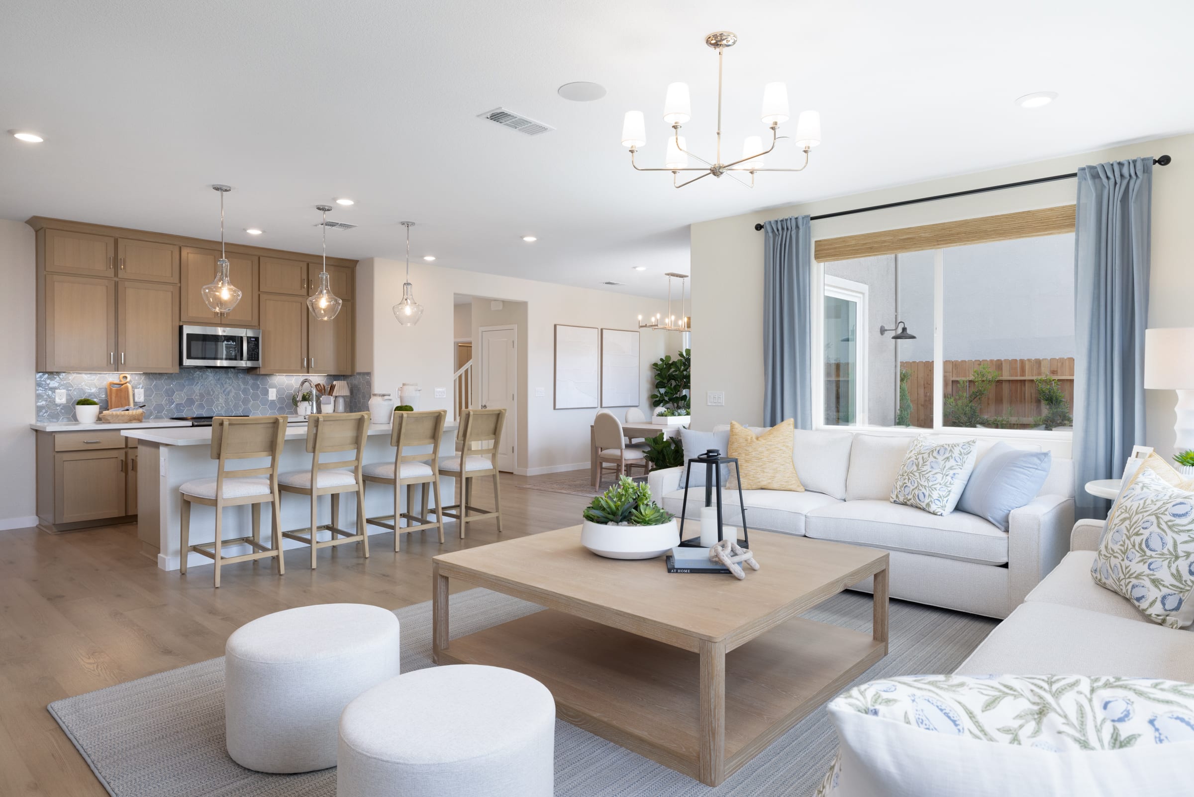 A modern living room with a large sectional sofa and coffee table in the foreground, and a kitchen with an island and dining area in the background.