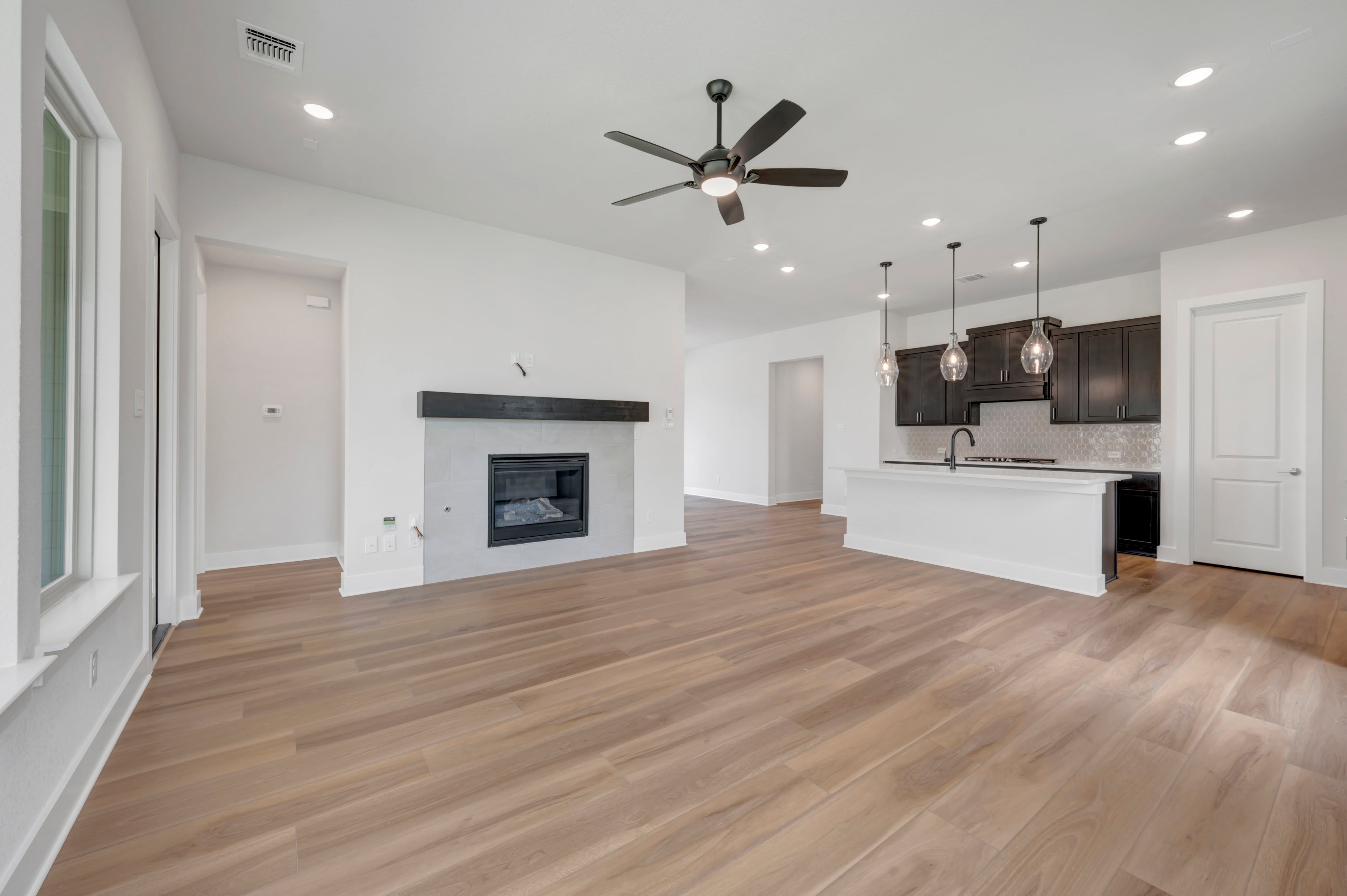 A modern living room with a fireplace in the foreground and a kitchen island with pendant lights in the background.