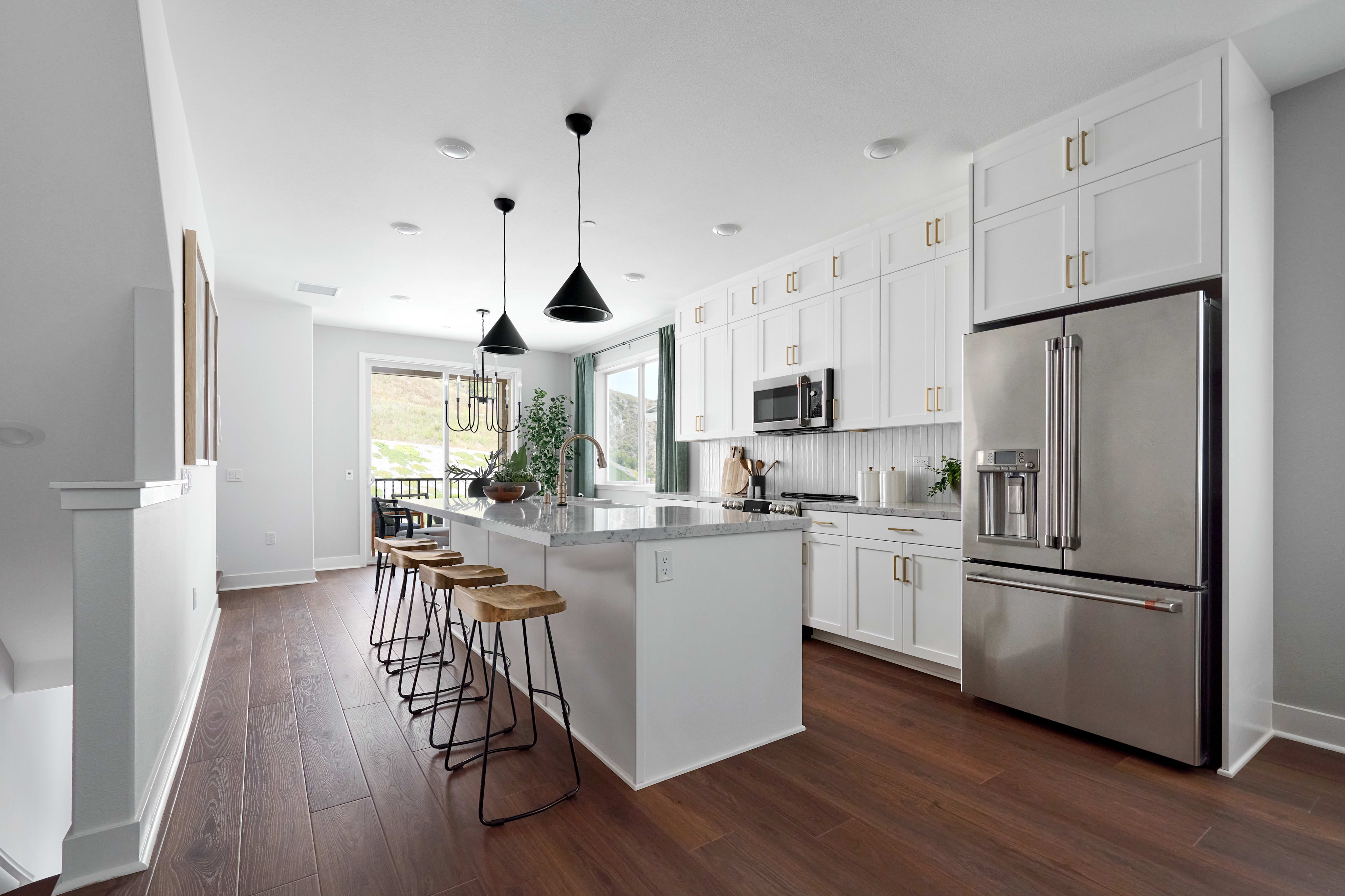 A modern kitchen with a large island and bar stools in the foreground and a stainless steel refrigerator and white cabinets in the background.