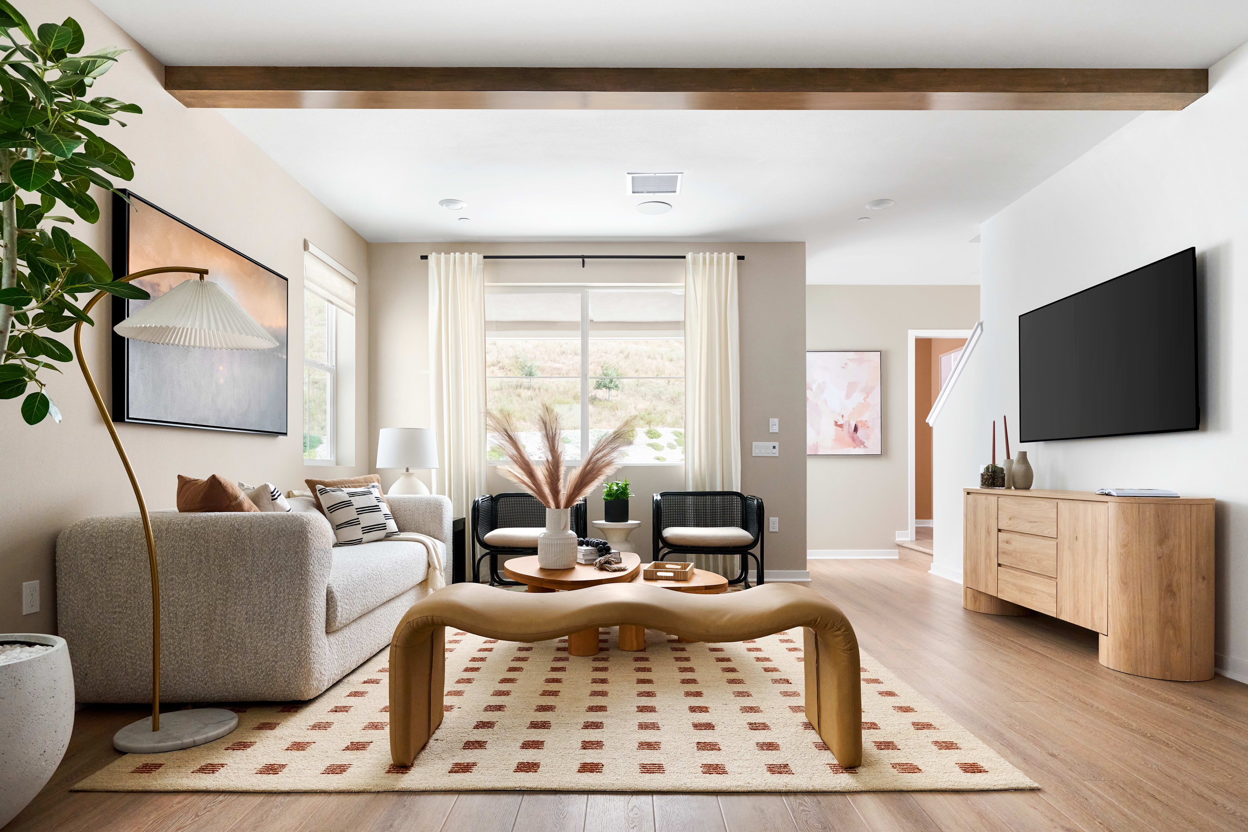 A modern living room with a curved wooden coffee table and a plush sofa in the foreground, and a television and staircase in the background.