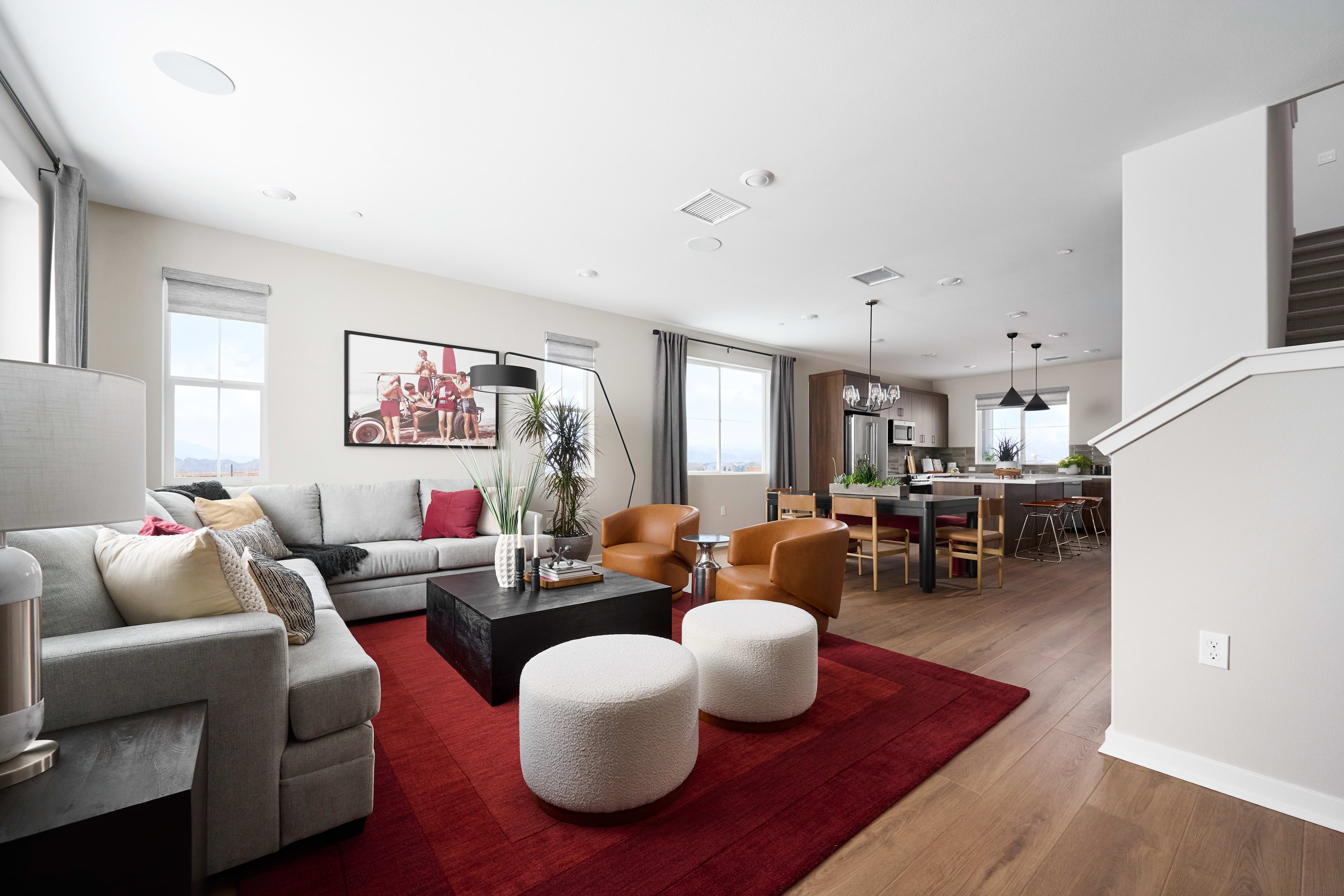A spacious living room with a sectional sofa and red rug in the foreground opens to a modern kitchen and dining area in the background.