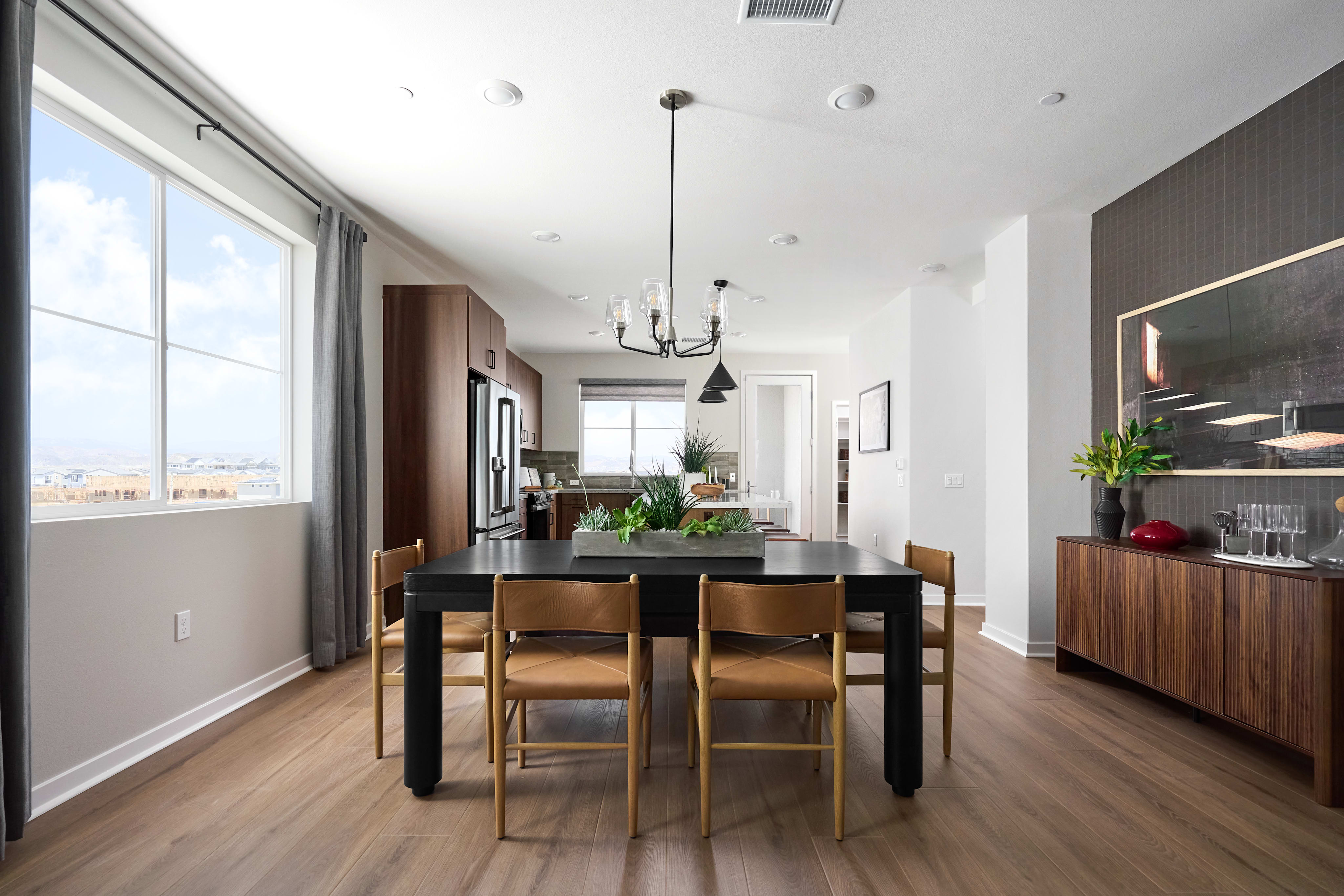 A modern dining room with a dark table and leather chairs in the foreground, and a kitchen and living area with a textured accent wall in the background.