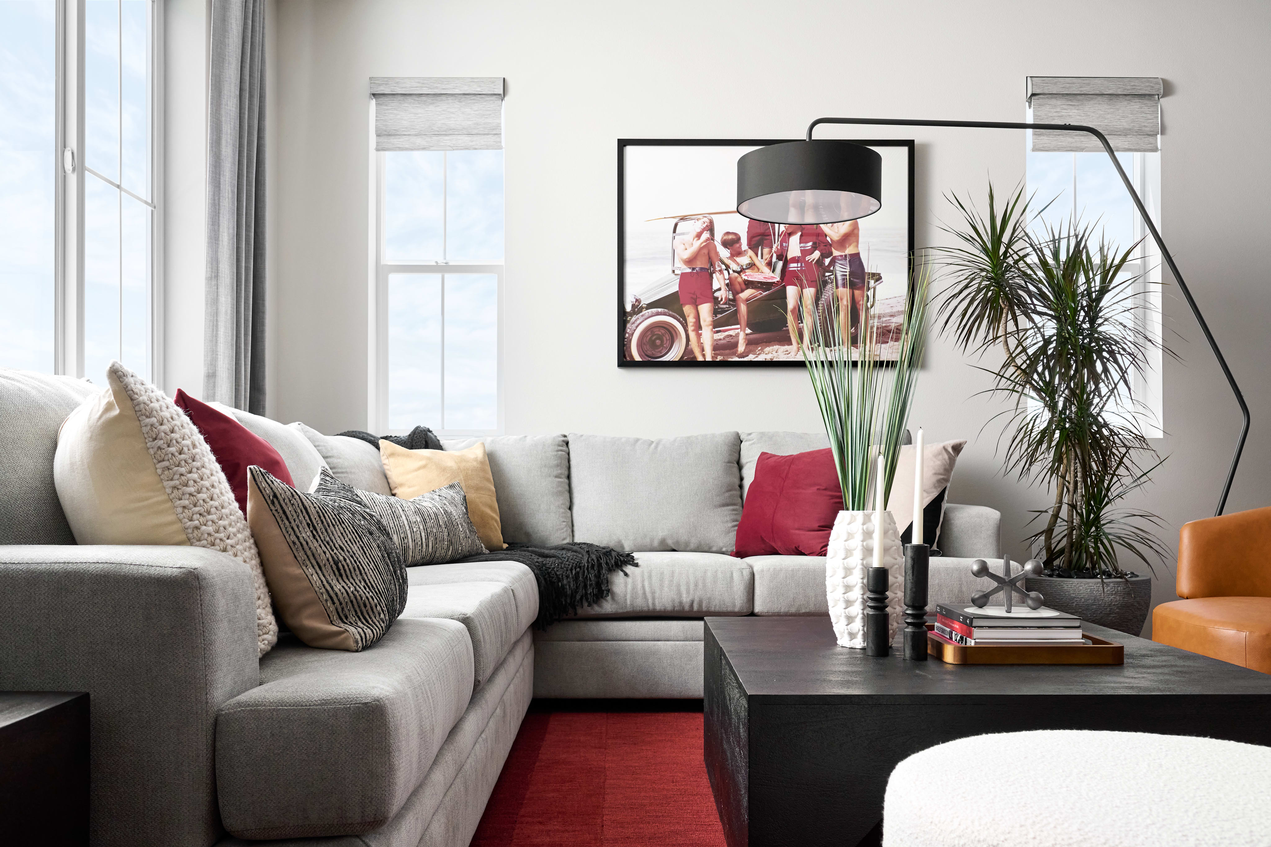 A large gray sectional sofa with colorful pillows sits in the foreground, facing a black coffee table and a large framed vintage photograph on the wall in the background.